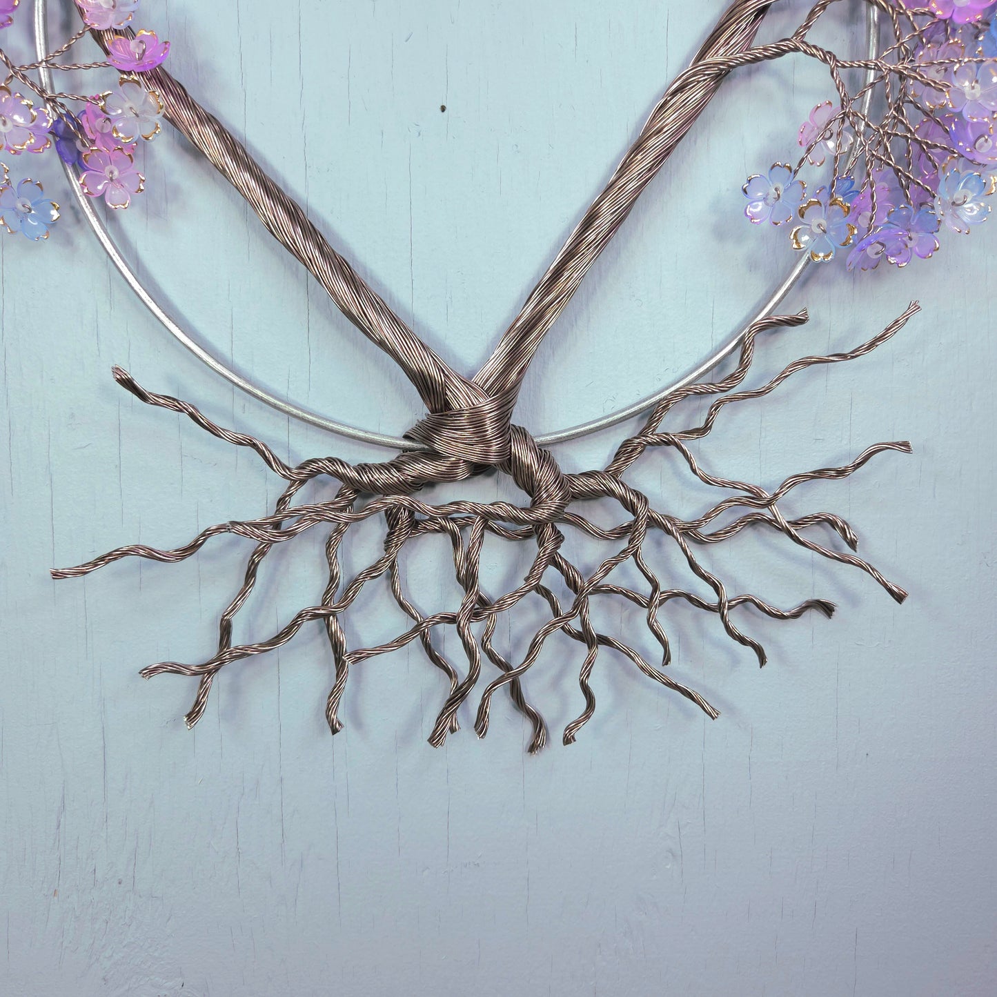 Decorative wall art with twisted metal branches and purple flowers on a light blue background