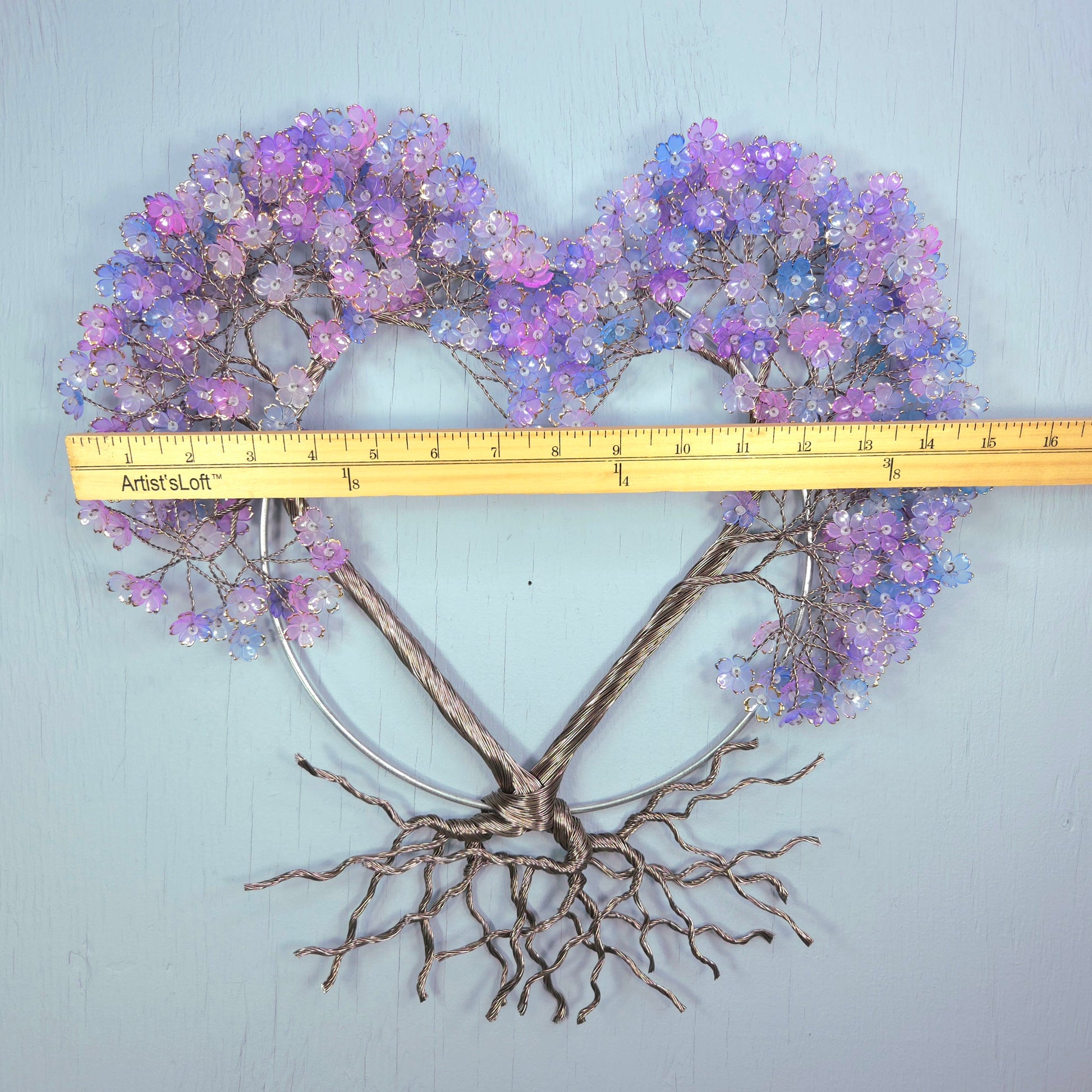 Heart-shaped decorative piece with purple flowers and bare branches, measured against a ruler on a light blue background.