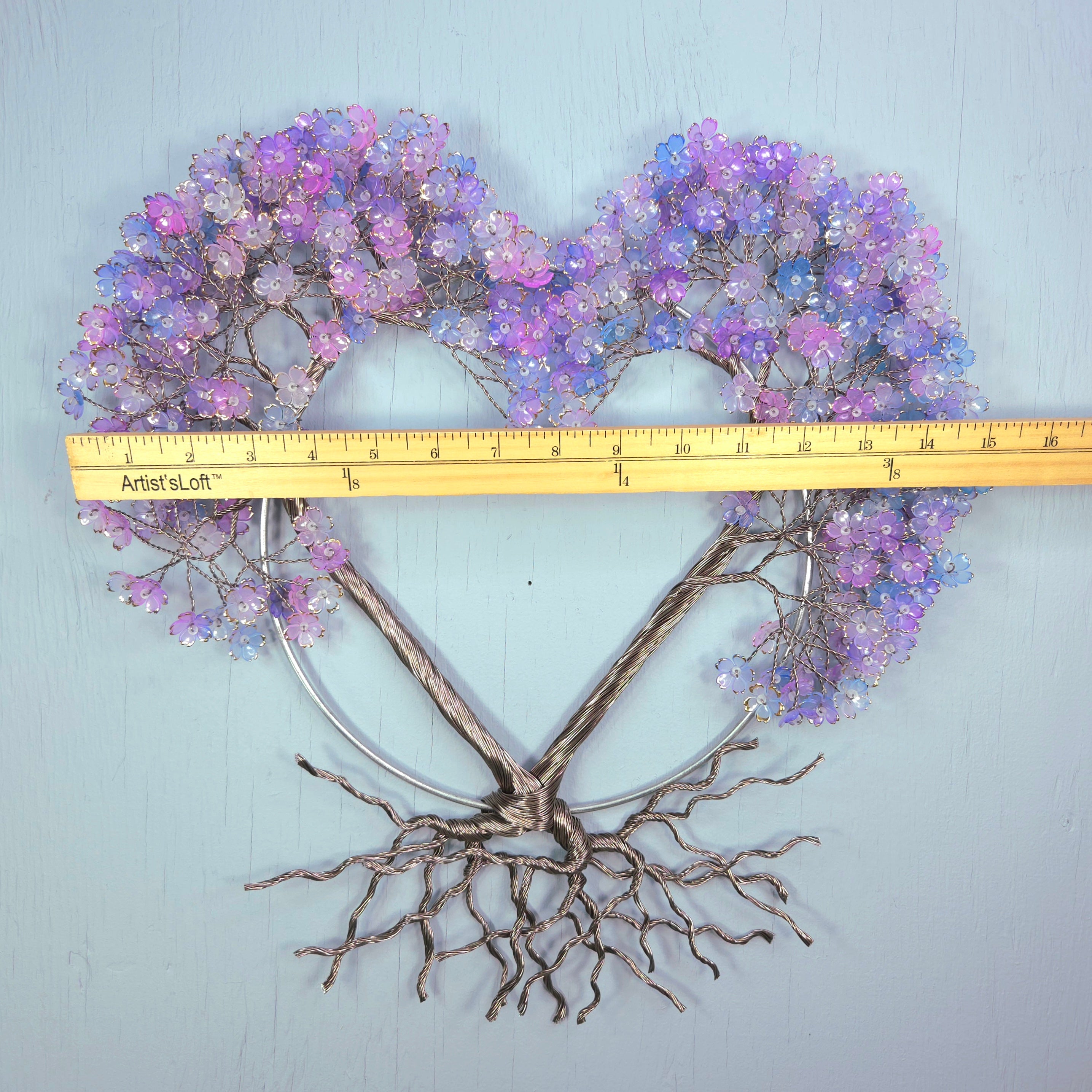 Heart-shaped decorative piece with purple flowers and bare branches, measured against a ruler on a light blue background.