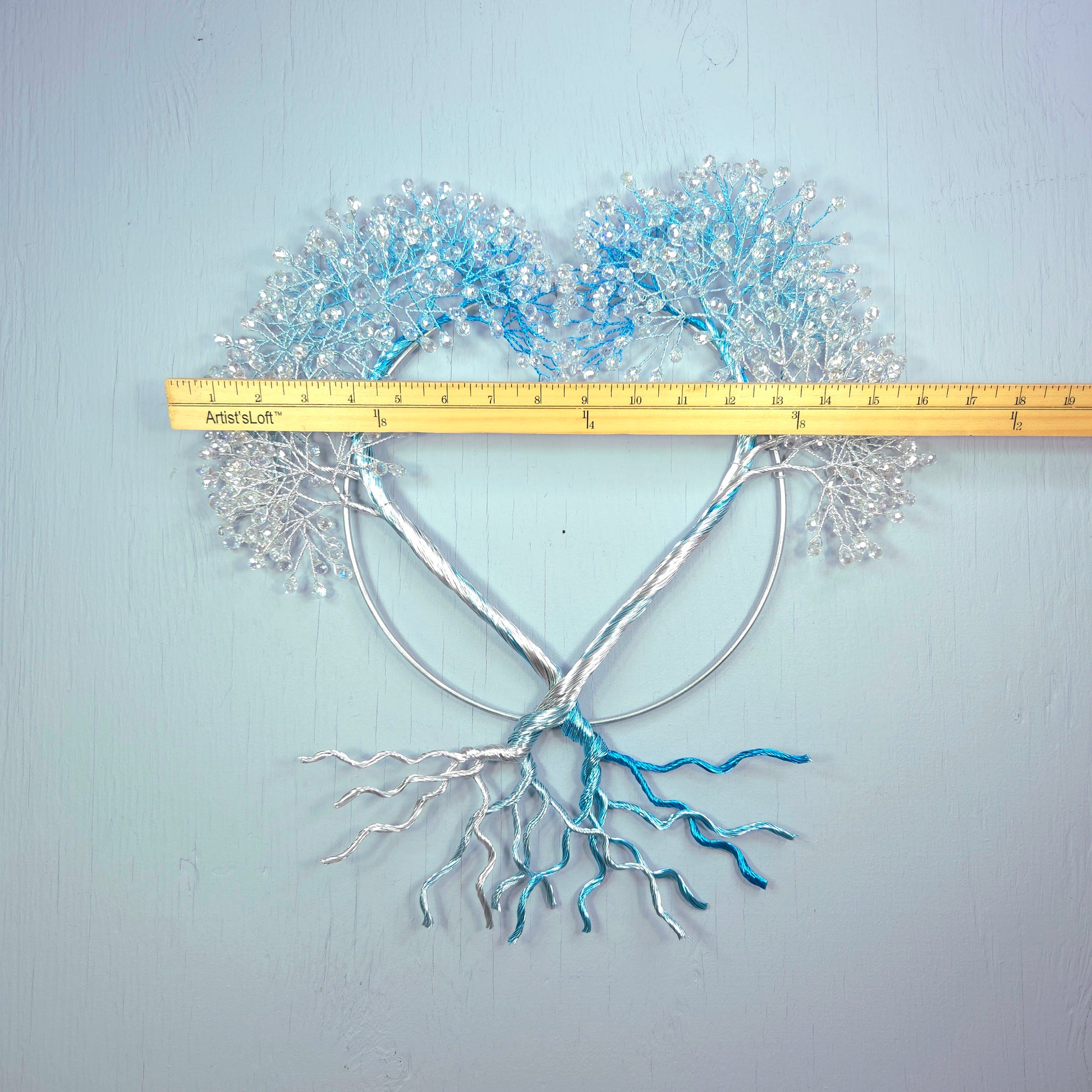Decorative metal tree with heart-shaped top and roots on a light blue background, measured by a ruler.