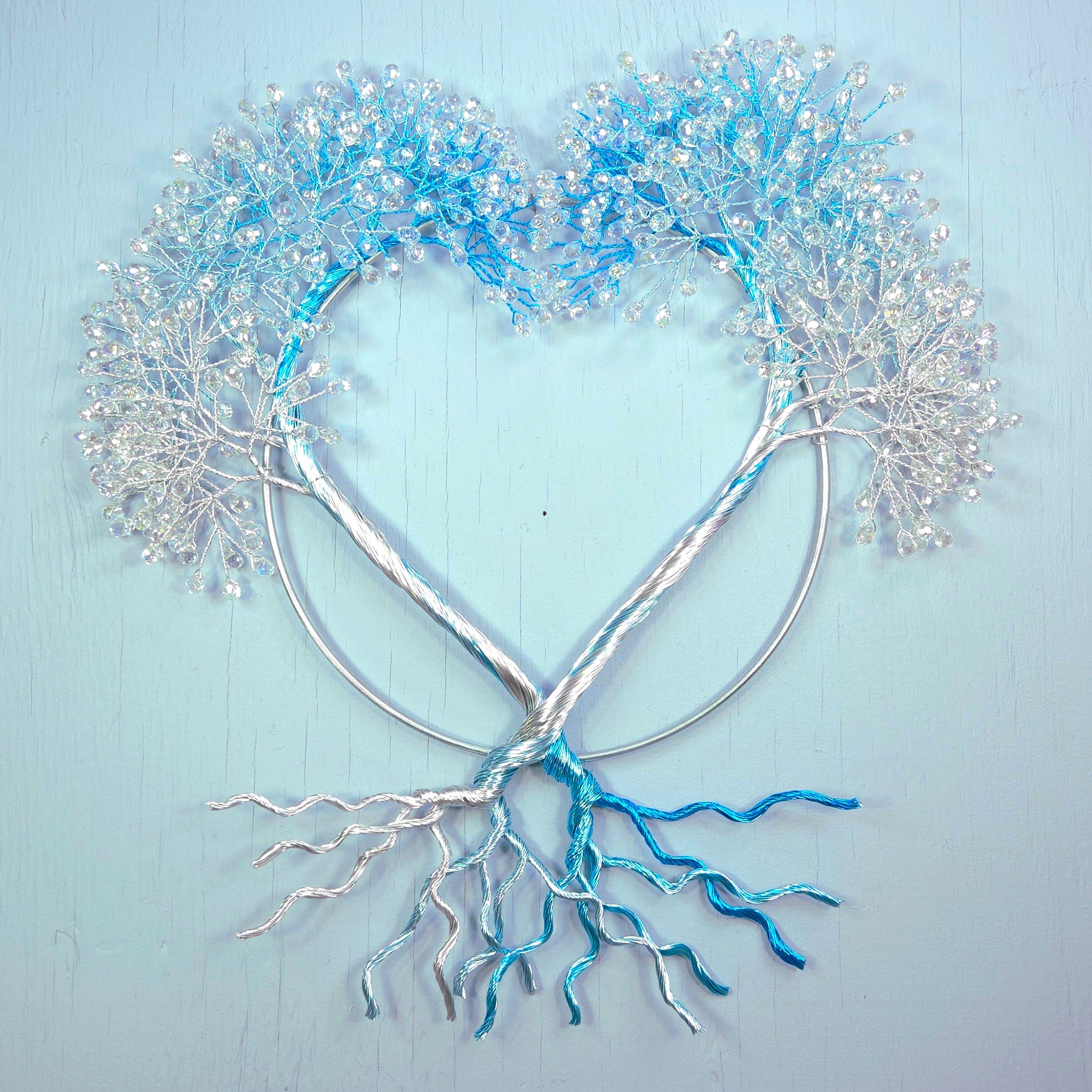 Heart-shaped metal sculpture with blue and silver branches on a light blue background