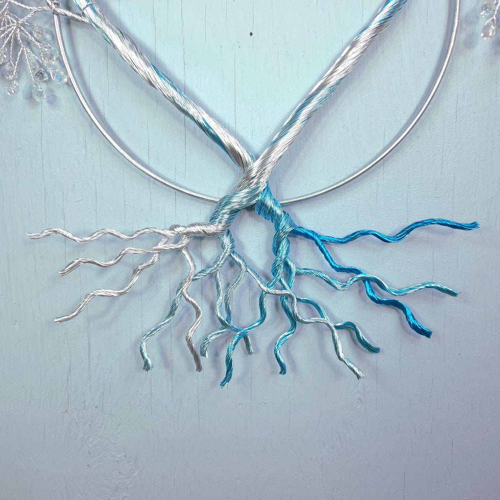 Metallic tree sculpture with branches and roots on a light blue background