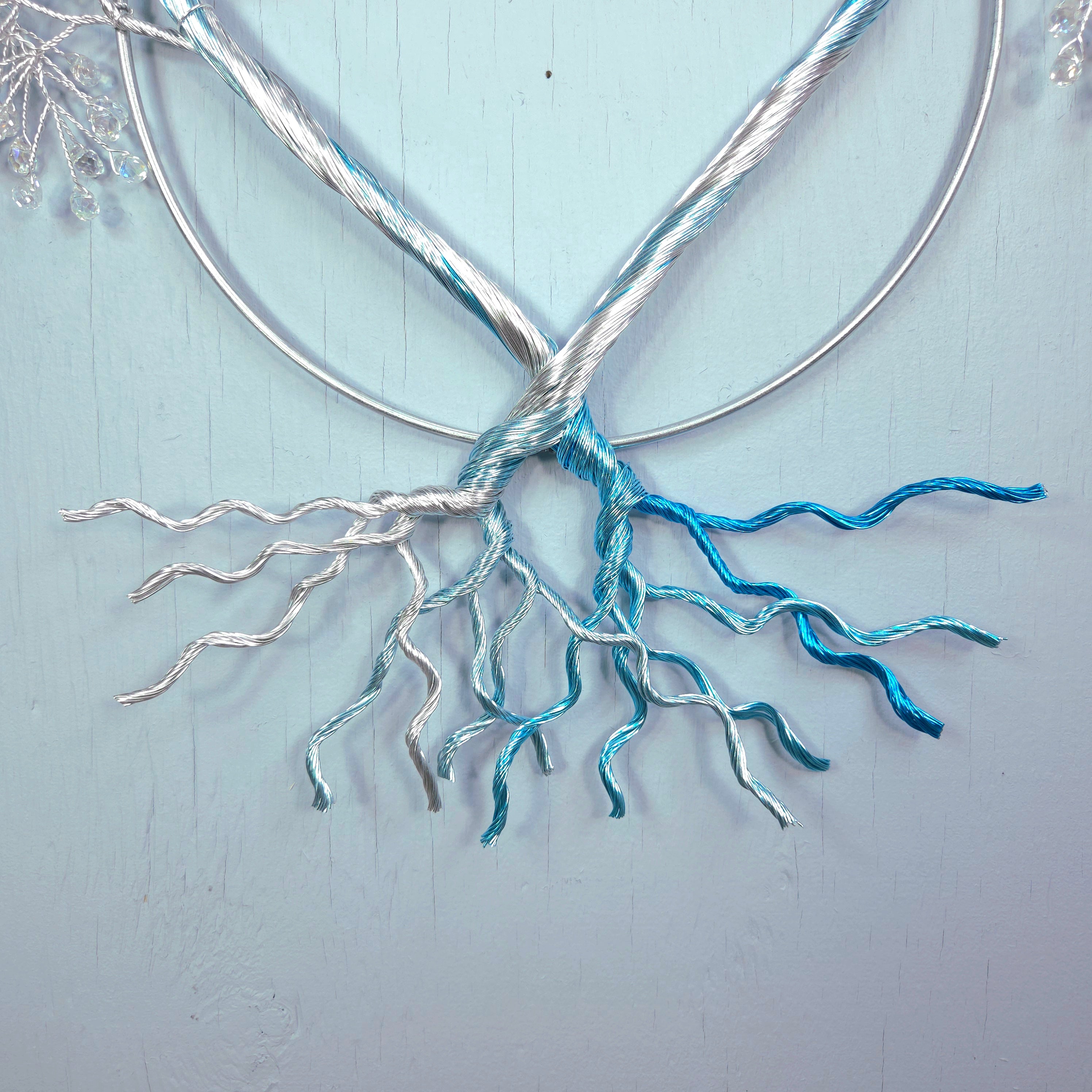 Metallic tree sculpture with branches and roots on a light blue background
