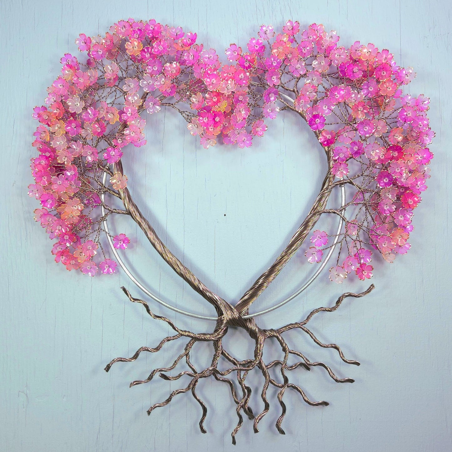 Decorative wall art with pink floral branches and root-like base on a light blue background