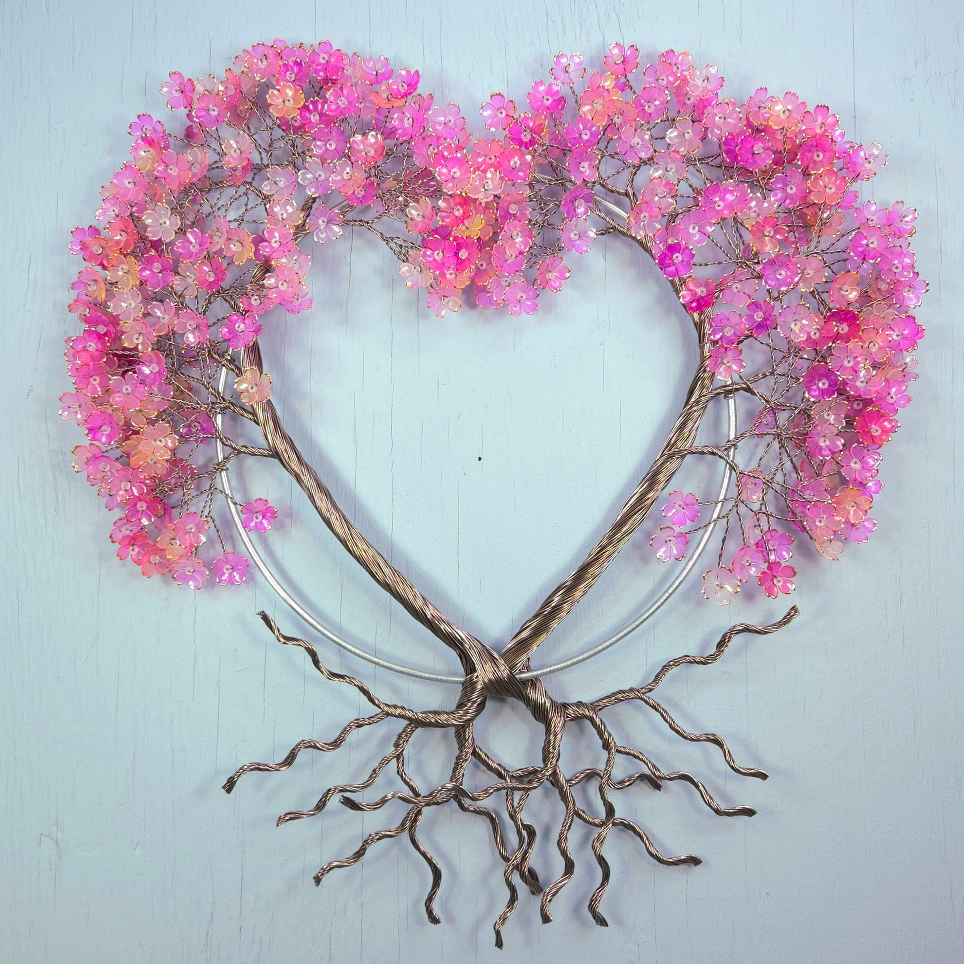 Decorative wall art with pink floral branches and root-like base on a light blue background