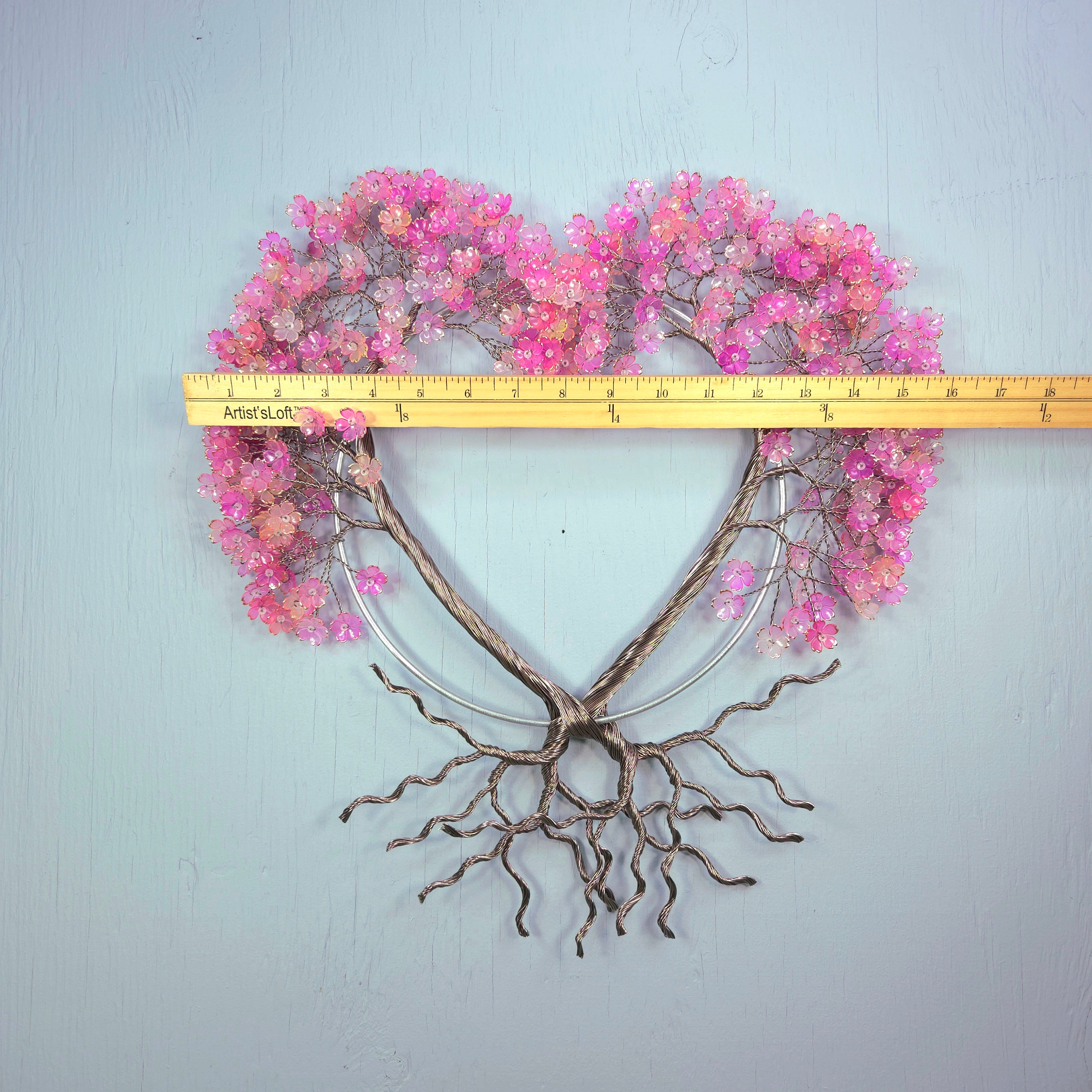 Heart-shaped decorative wall piece with pink flowers and bare branches, measured against a ruler.