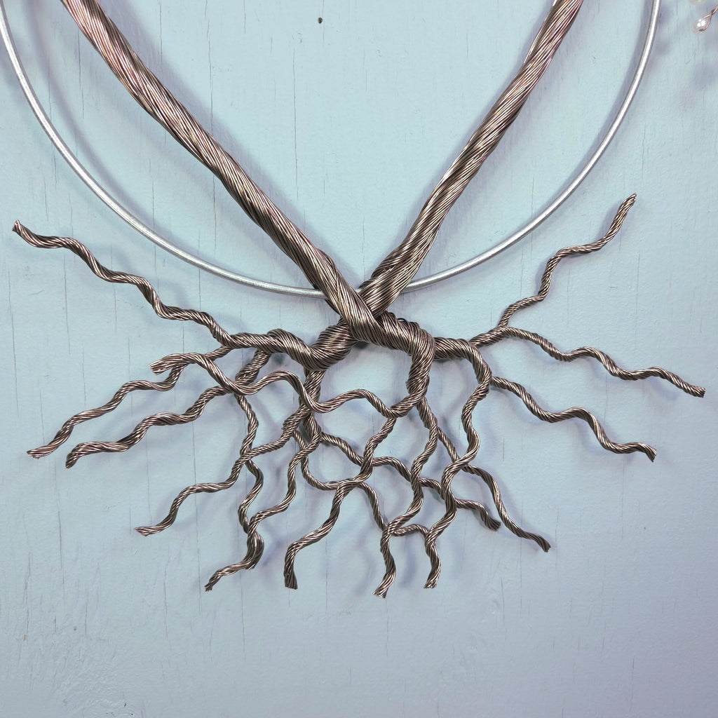 Metallic wire sculpture resembling roots on a light blue background