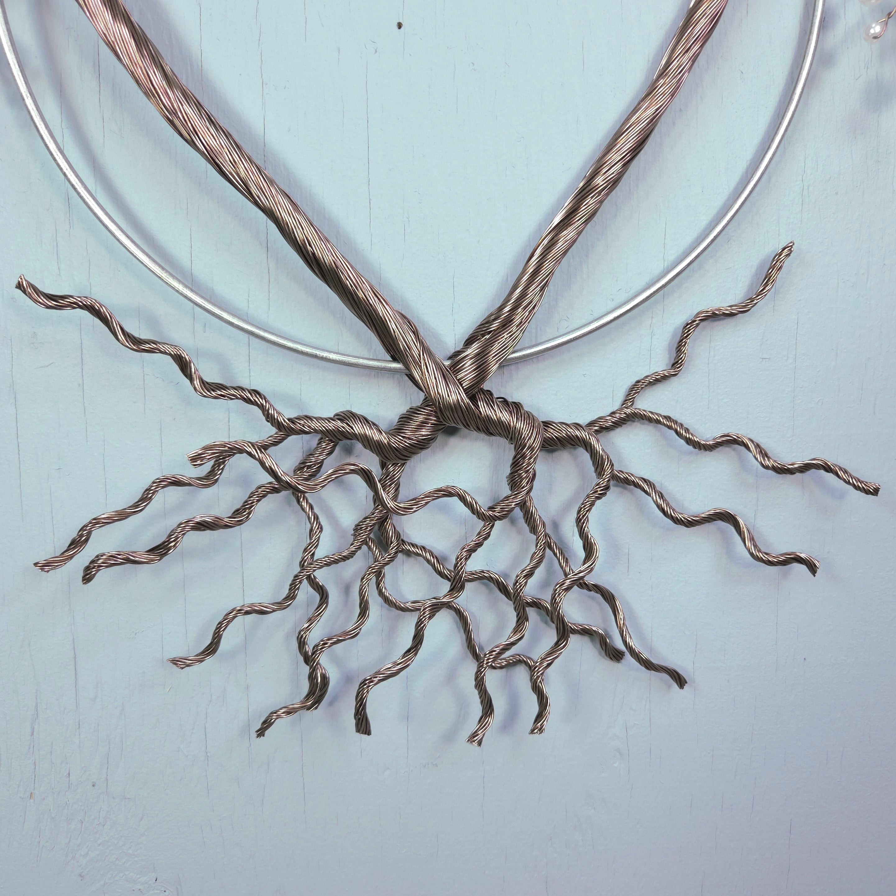Metallic wire sculpture resembling roots on a light blue background