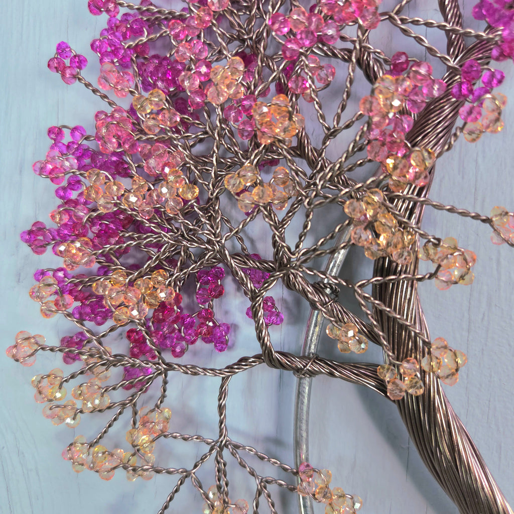Decorative wall art with pink and orange beaded flowers on a light blue background