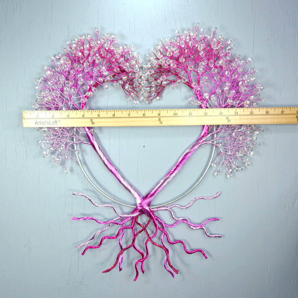 Heart-shaped arrangement of pink and white decorative elements with a ruler for scale on a light gray background.