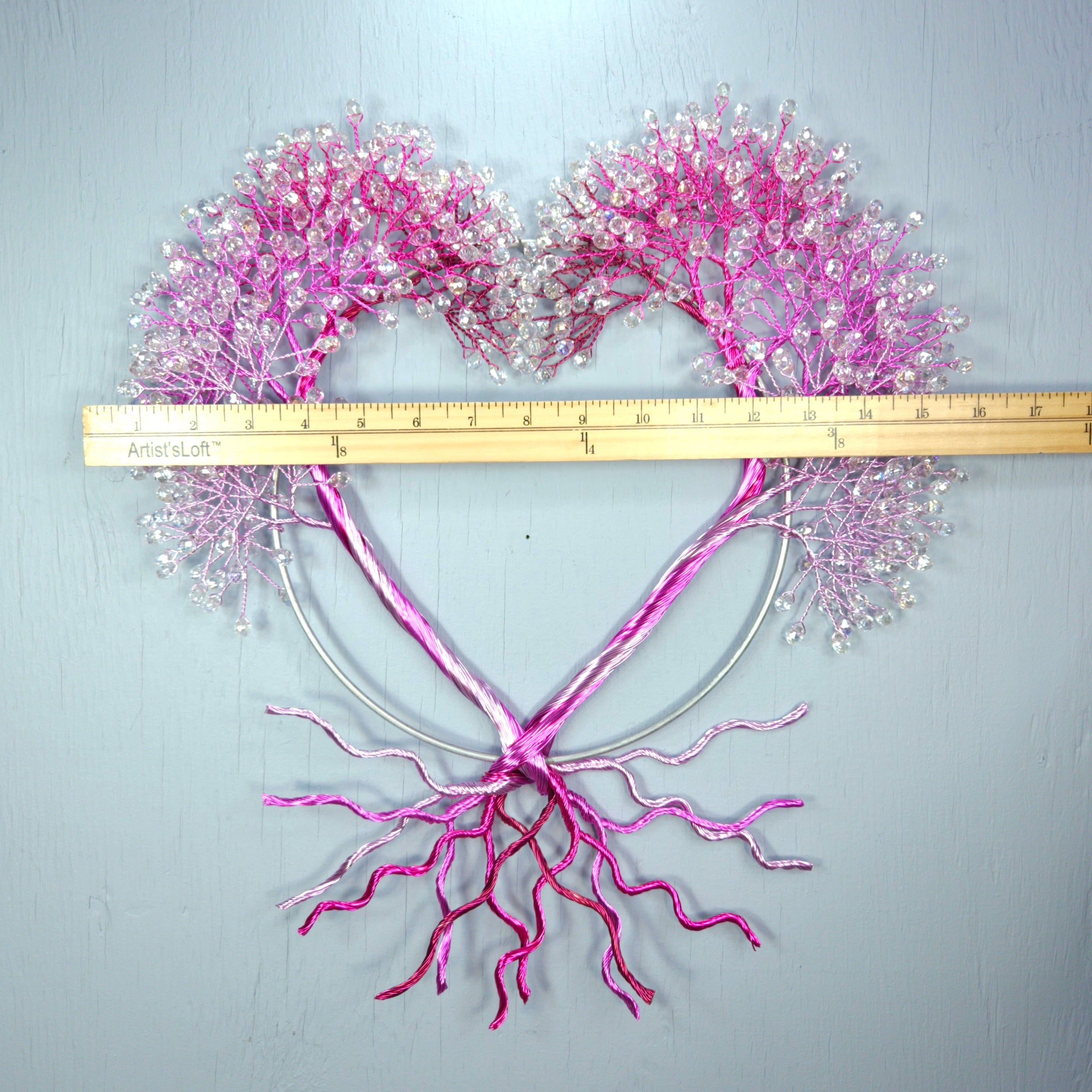 Heart-shaped arrangement of pink and white decorative elements with a ruler for scale on a light gray background.
