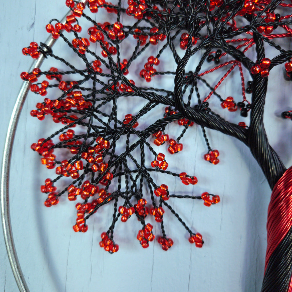 Close-up of a beaded tree art piece with red beads and black wires on a light blue background.