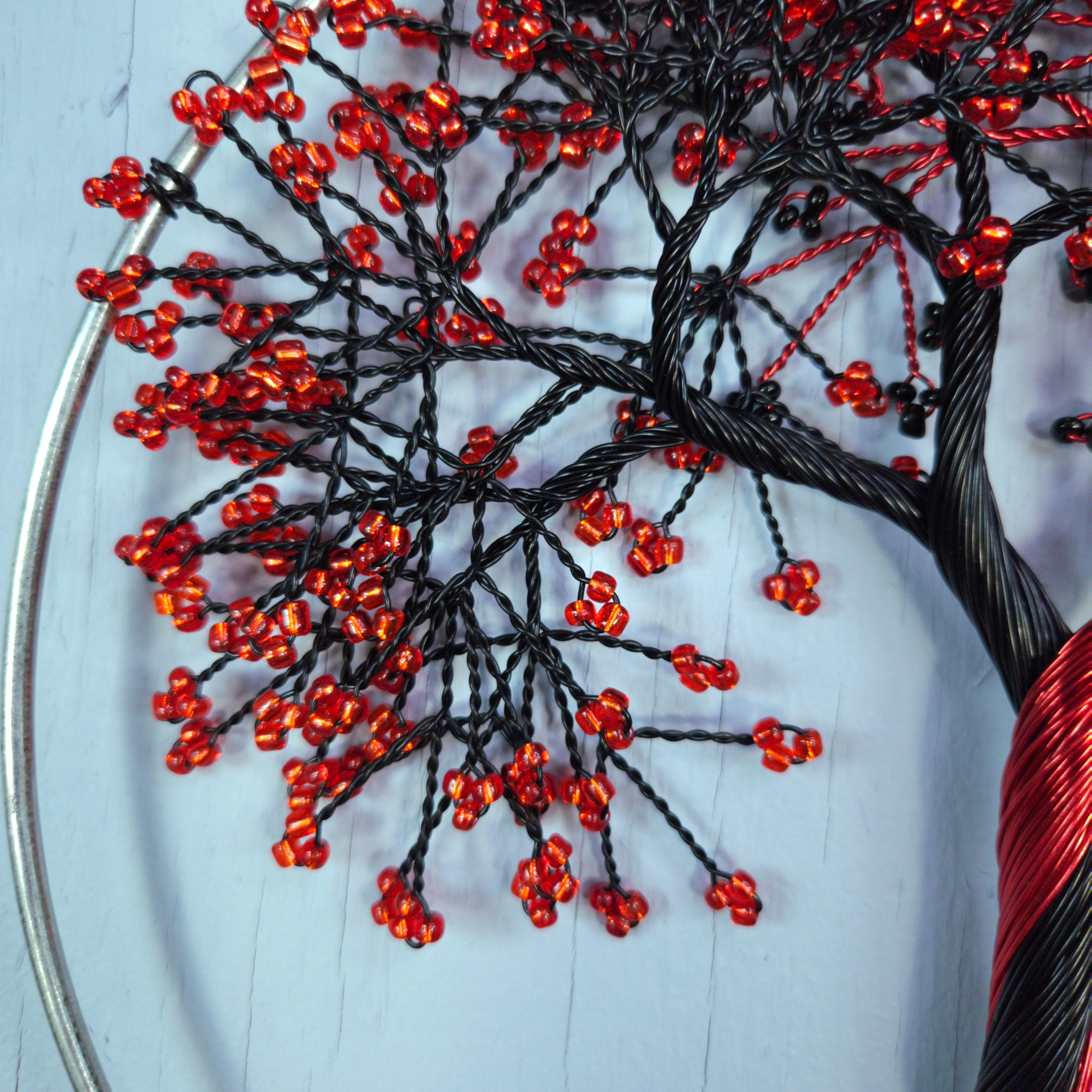 Close-up of a beaded tree art piece with red beads and black wires on a light blue background.