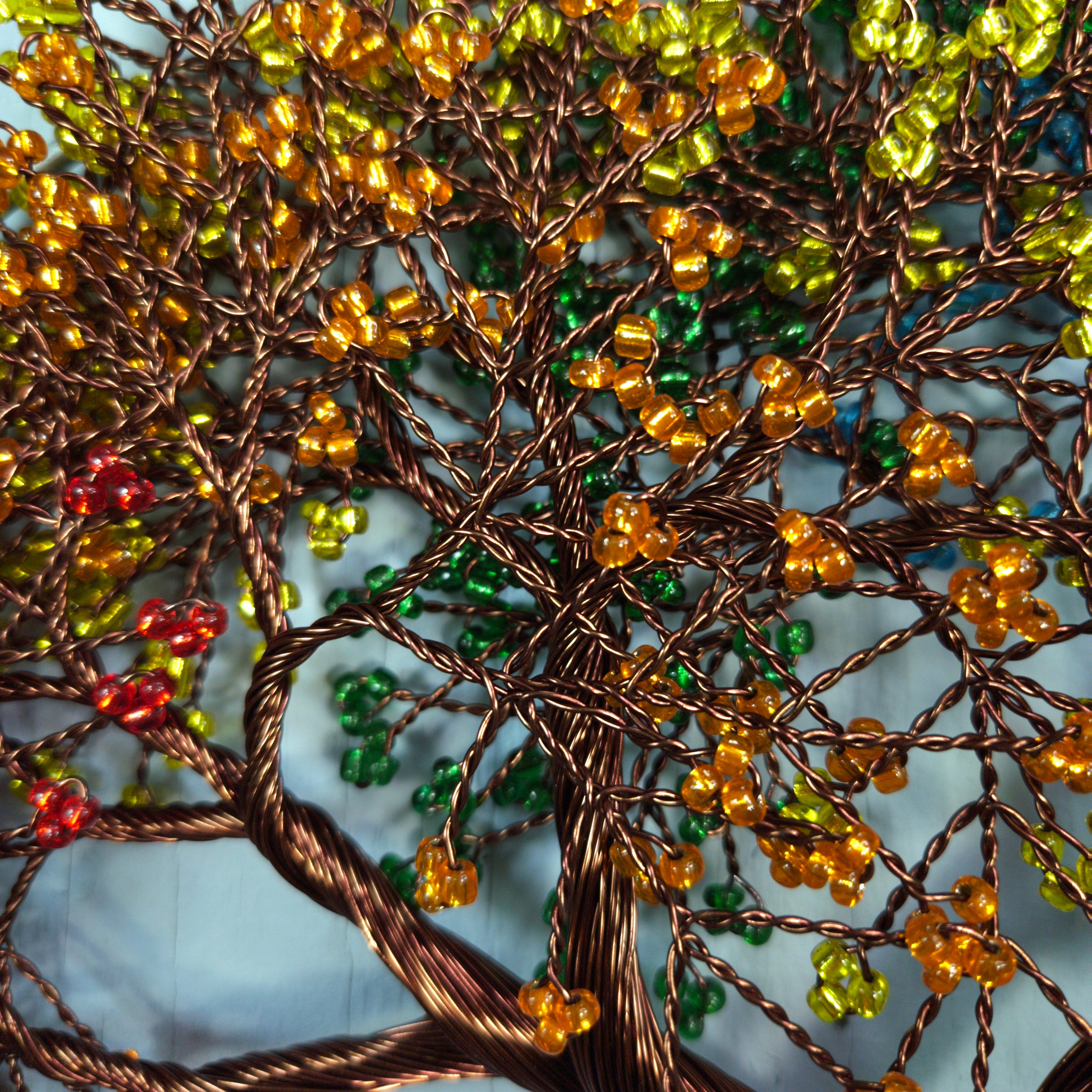 Close-up of a beaded tree sculpture with brown, green, and red beads on a textured background.