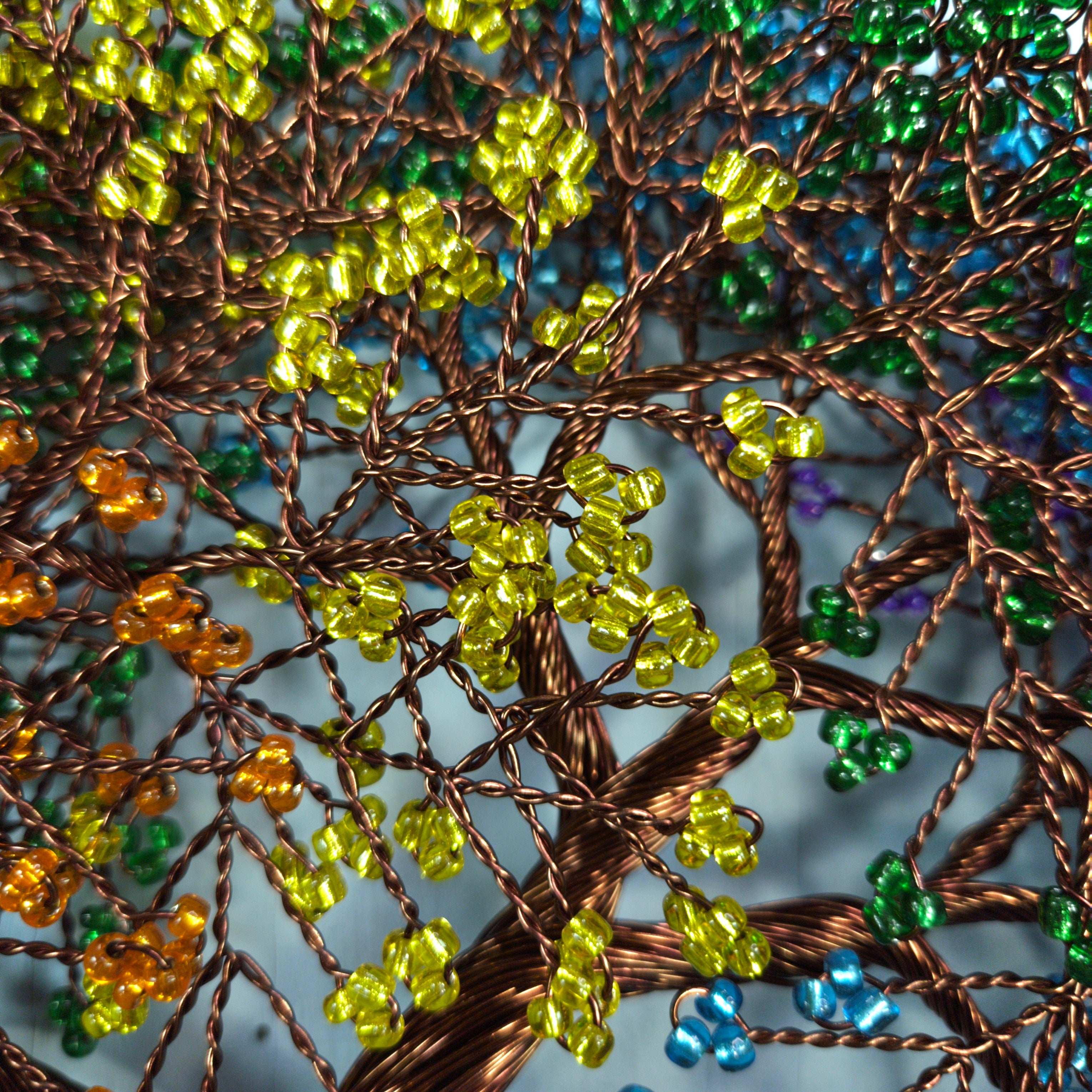 Close-up of a beaded tree with green, yellow, and blue beads on a textured background