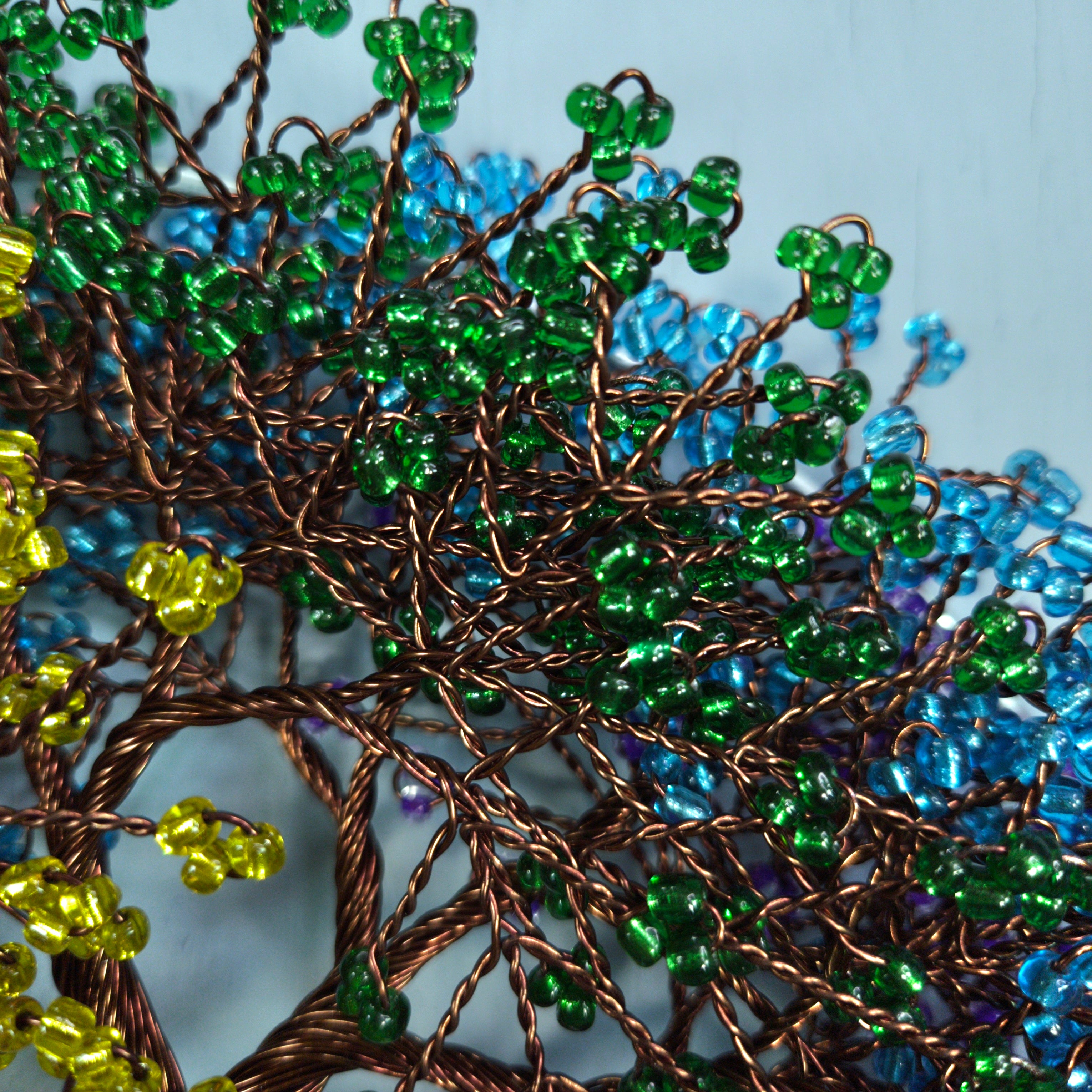 Close-up of a beaded tree sculpture with green, blue, and yellow beads on a light blue background.