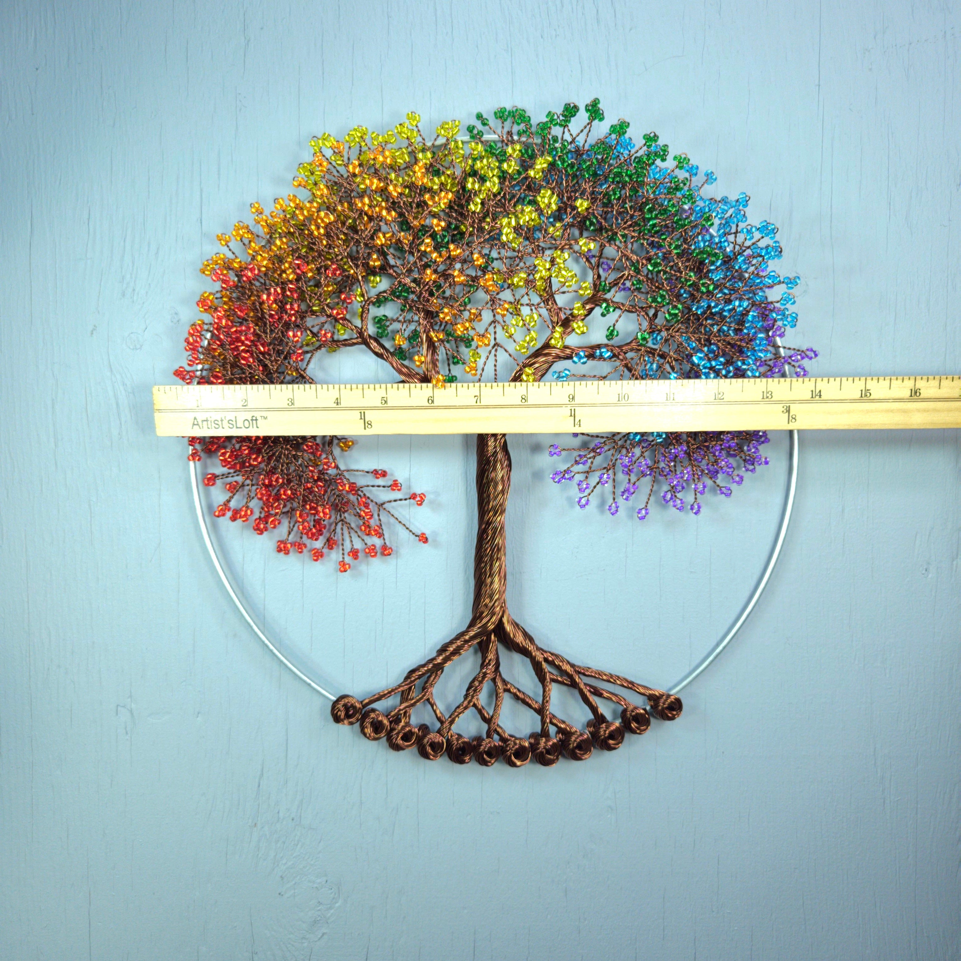 Decorative wall art of a tree with colorful leaves and a ruler for scale on a light blue background.