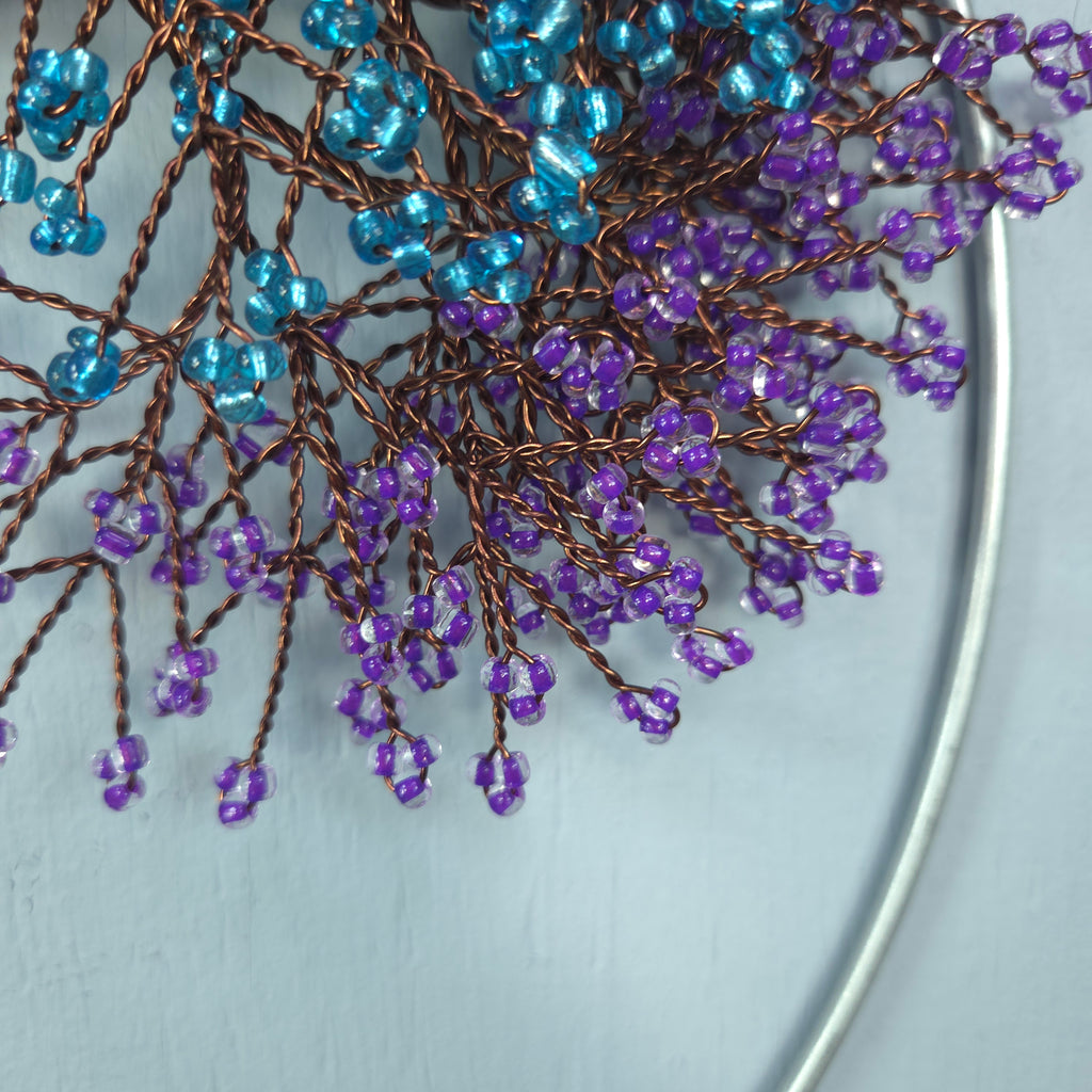 Close-up of blue and purple beaded branches on a light gray background