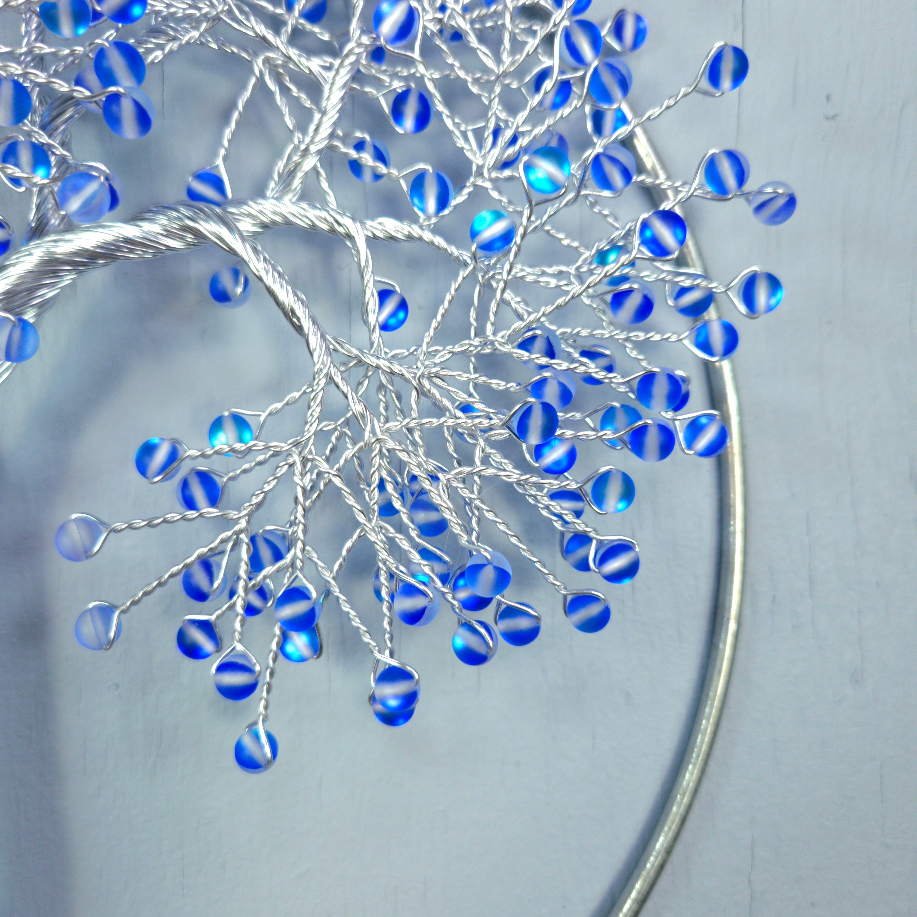 Decorative metal wall art with blue glass beads on a light gray background