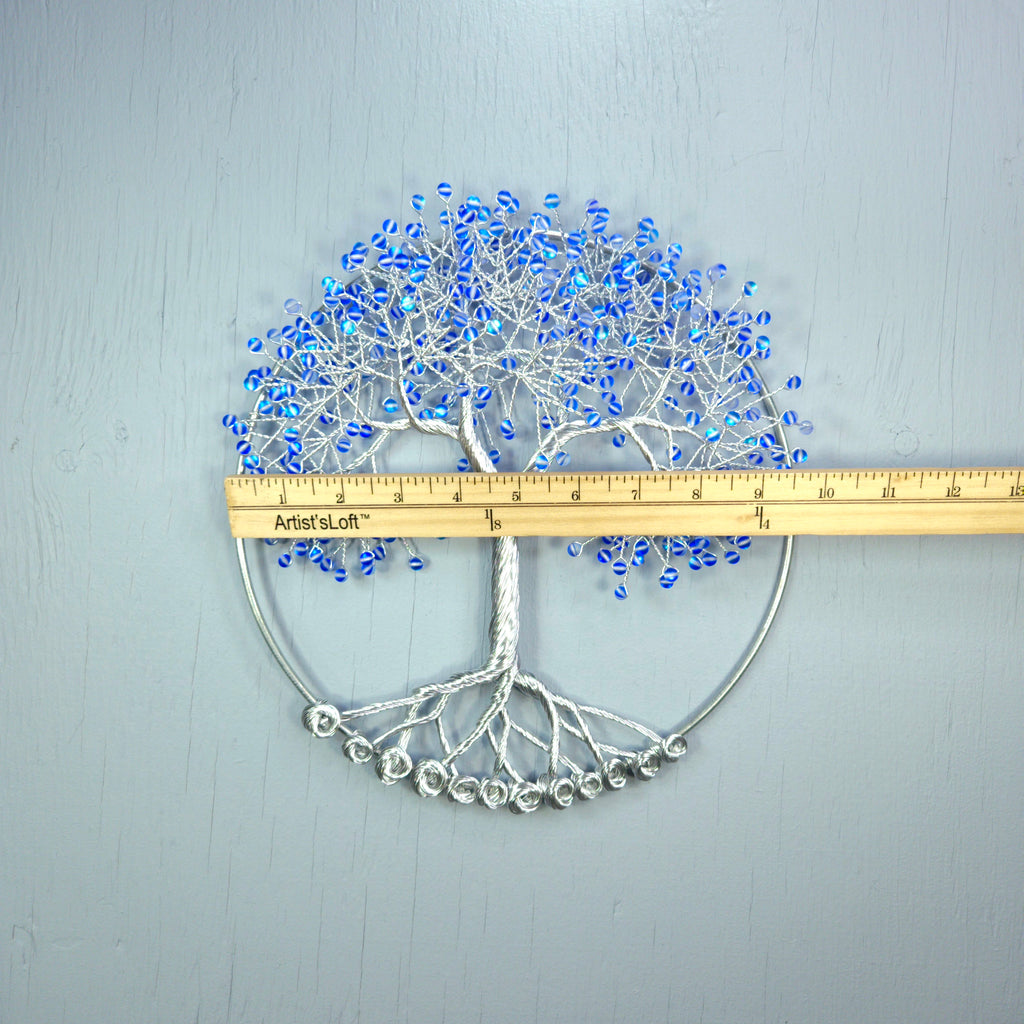 Decorative tree wall art with blue beads and a ruler for scale on a gray background
