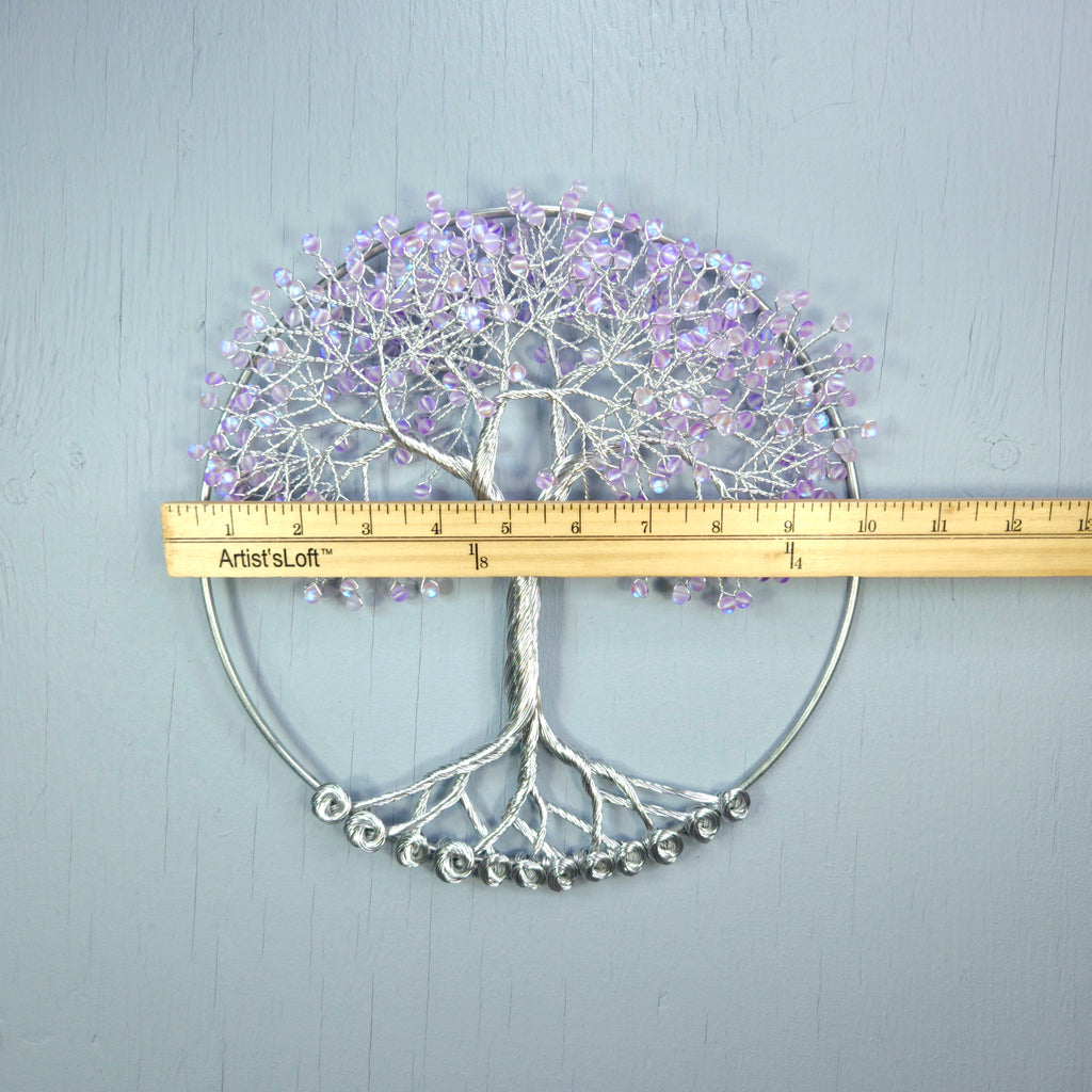Decorative wall art of a tree with purple flowers and silver base, measured against a ruler on a light gray background.
