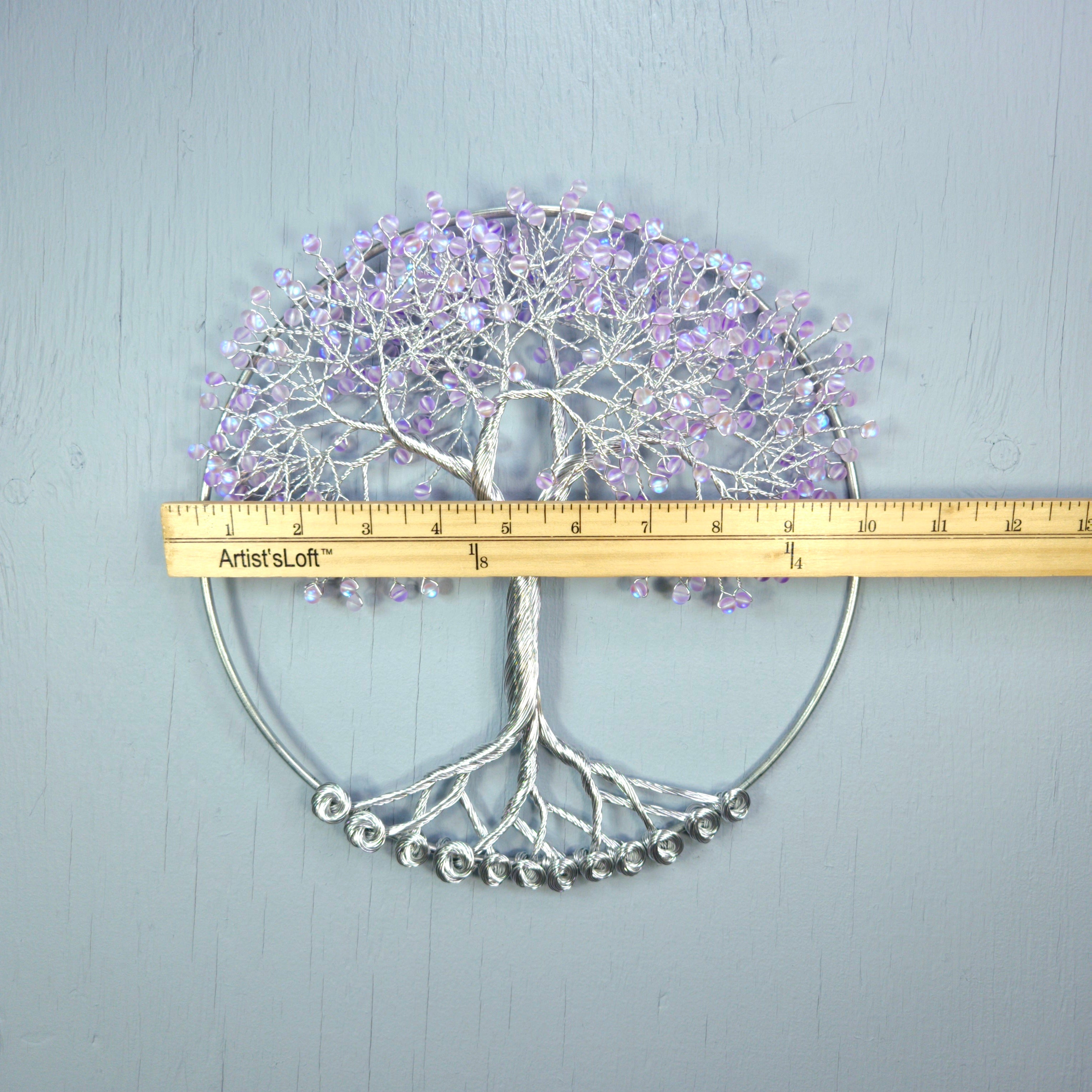 Decorative wall art of a tree with purple flowers and silver base, measured against a ruler on a light gray background.