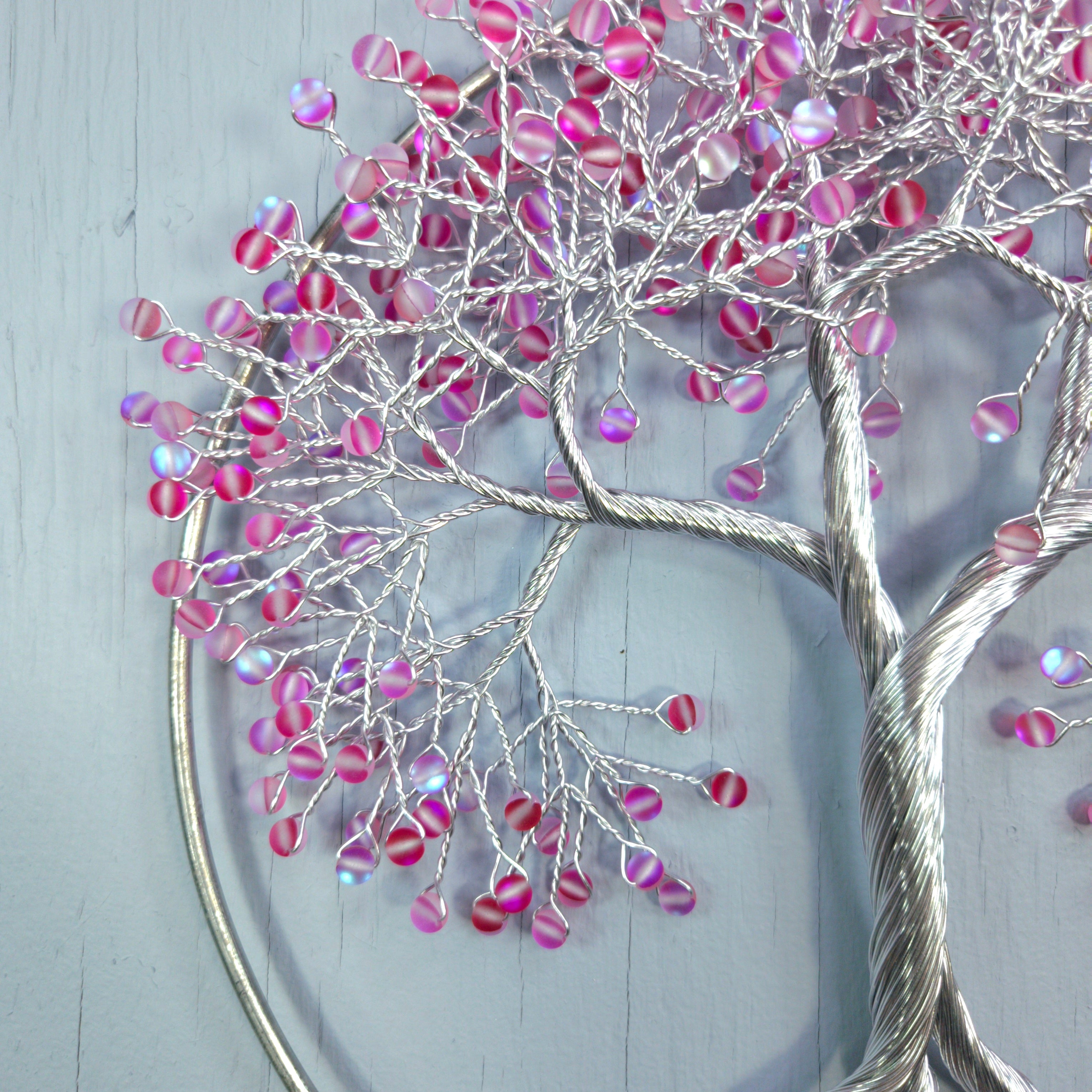 Decorative wall art with pink and purple beads on silver branches against a light gray background