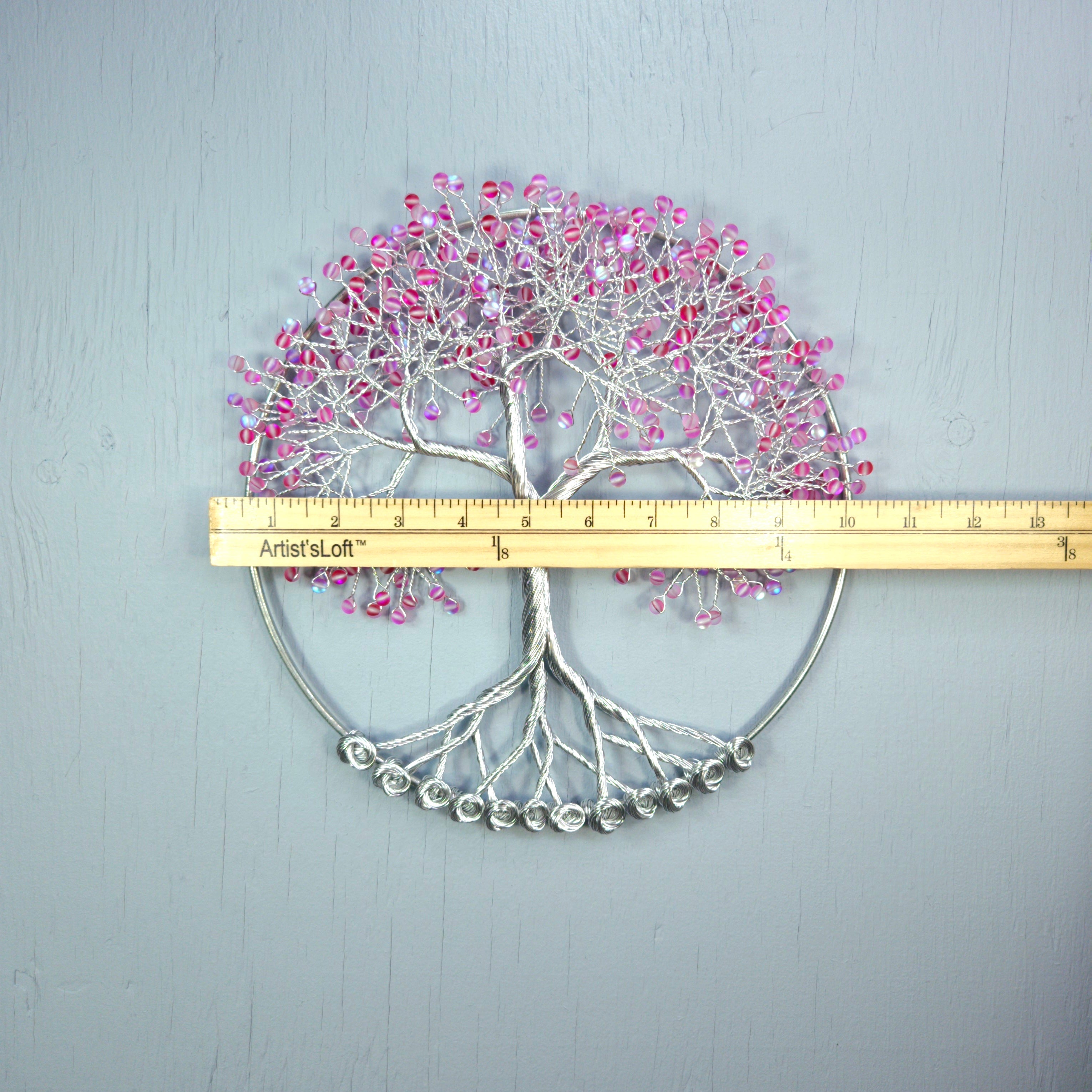 Decorative wall art with pink beads and a ruler for scale on a gray background