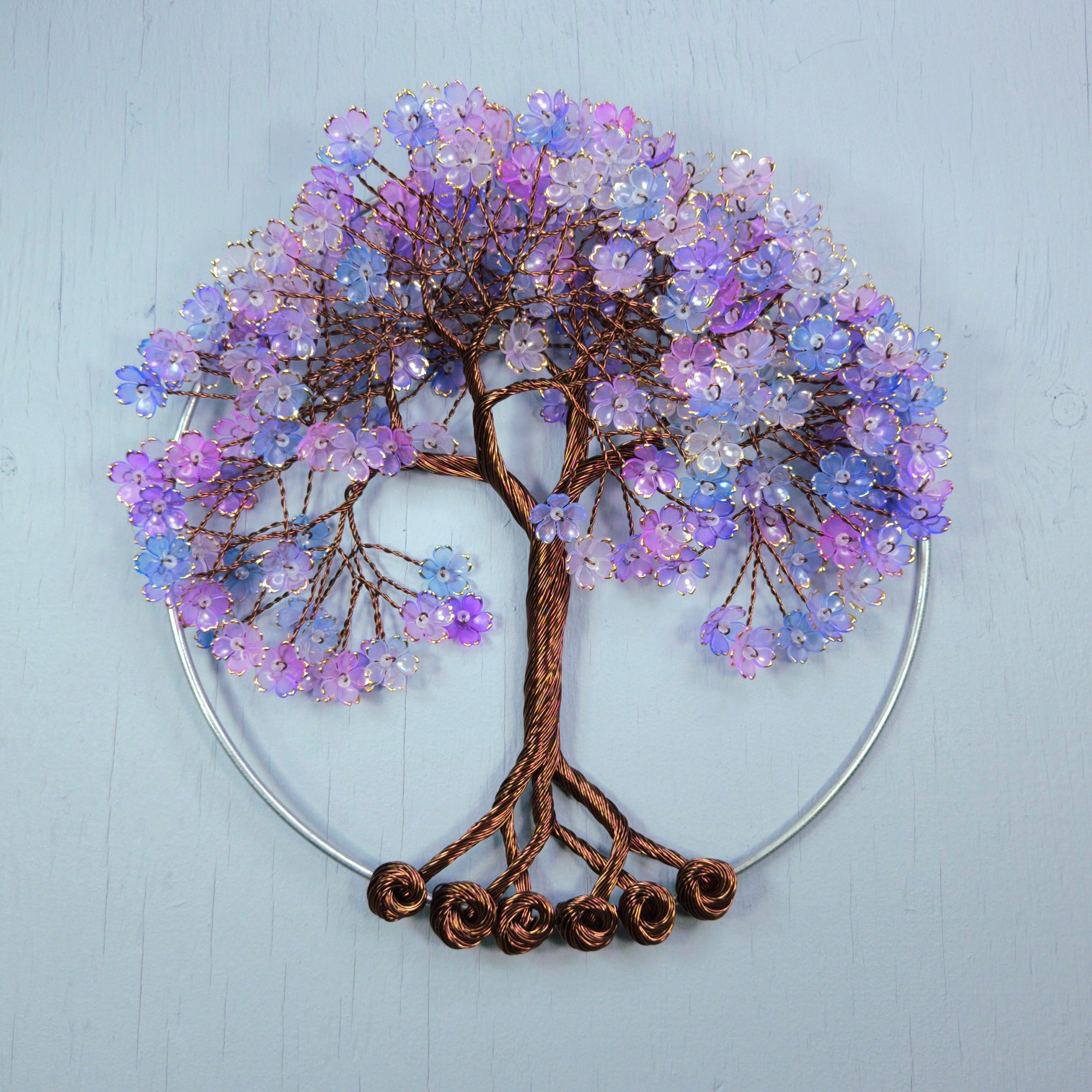 Decorative wall art of a tree with purple and blue flowers on a light blue background
