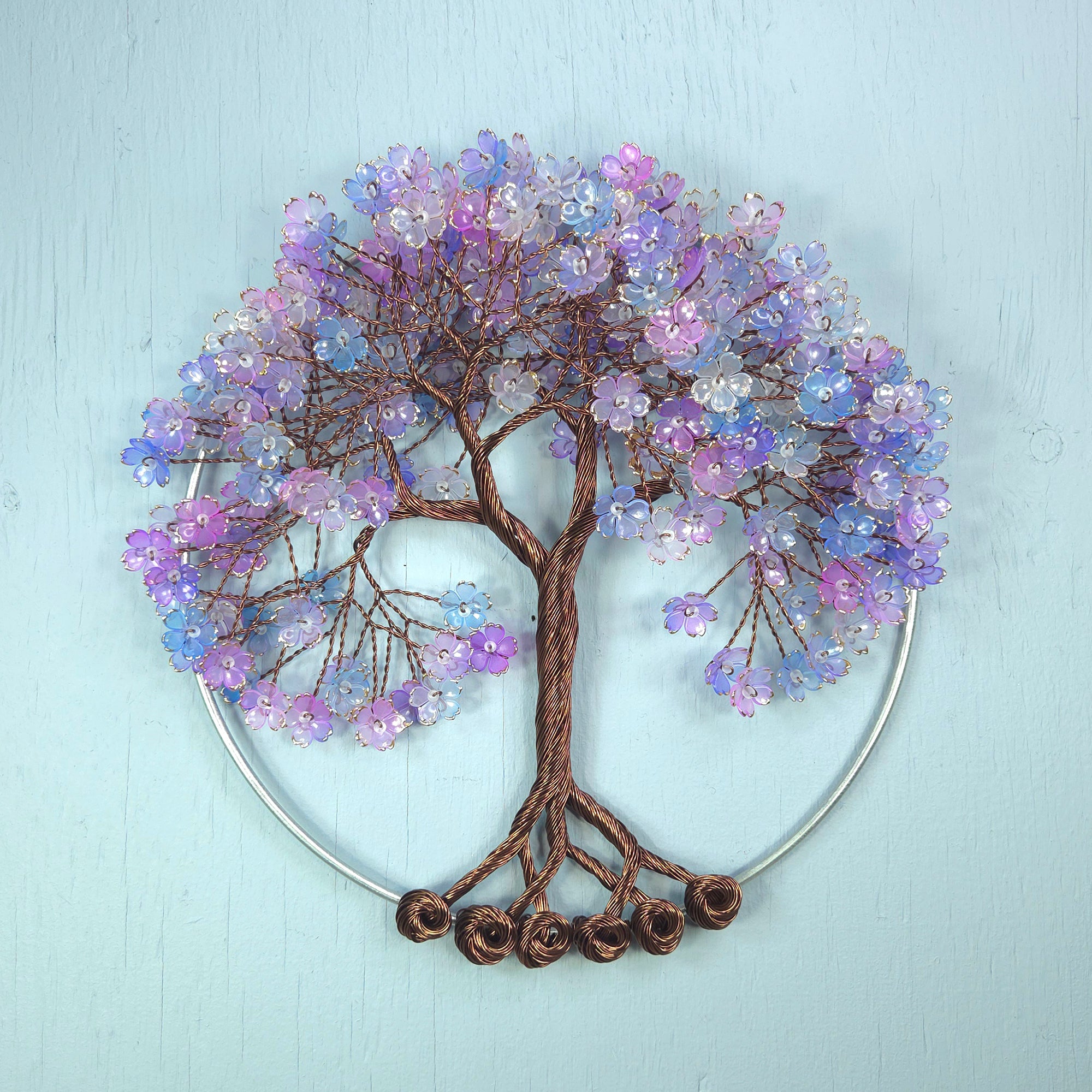 Decorative wall art of a tree with purple and blue flowers on a light blue background