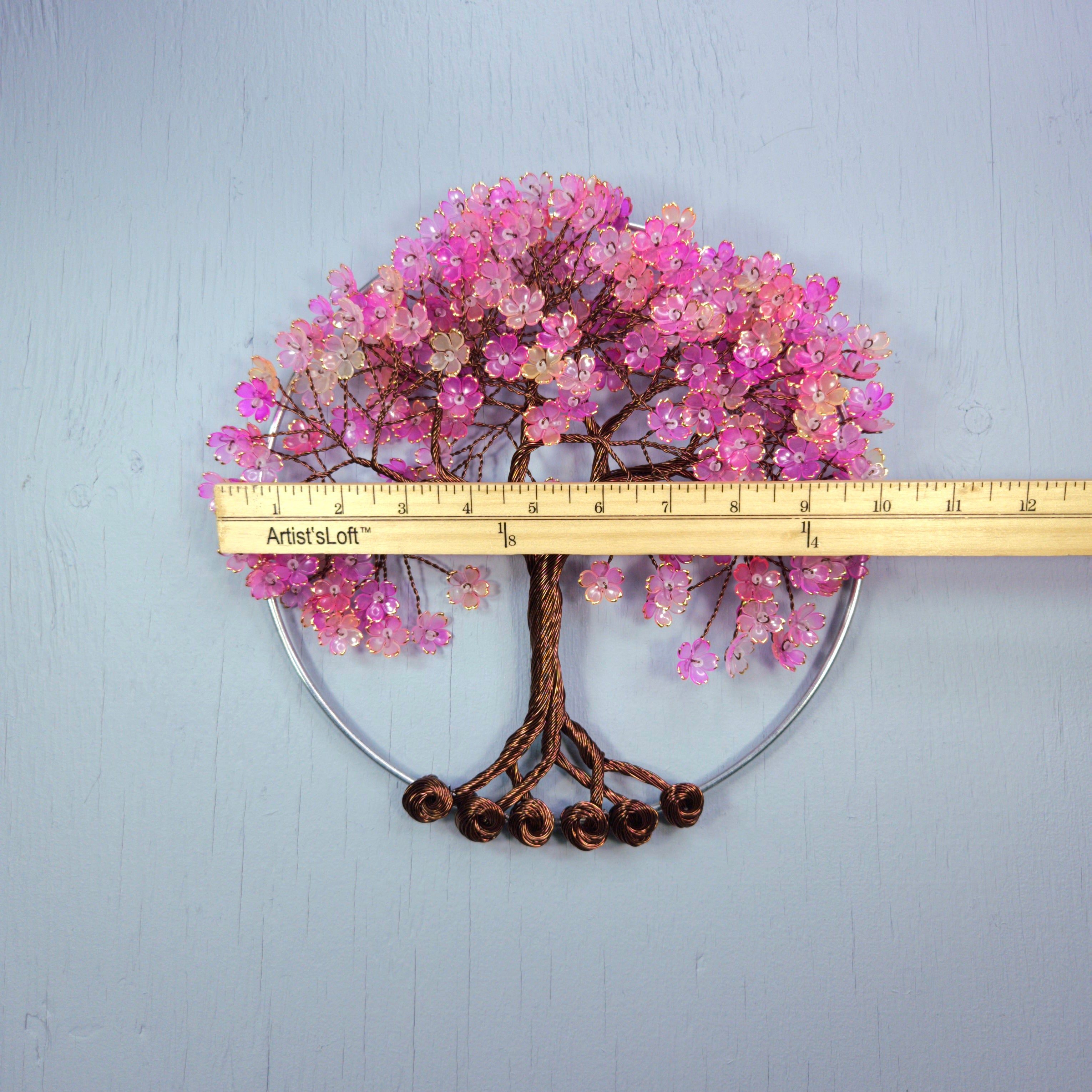 Decorative tree with pink flowers and a ruler for scale on a light blue background