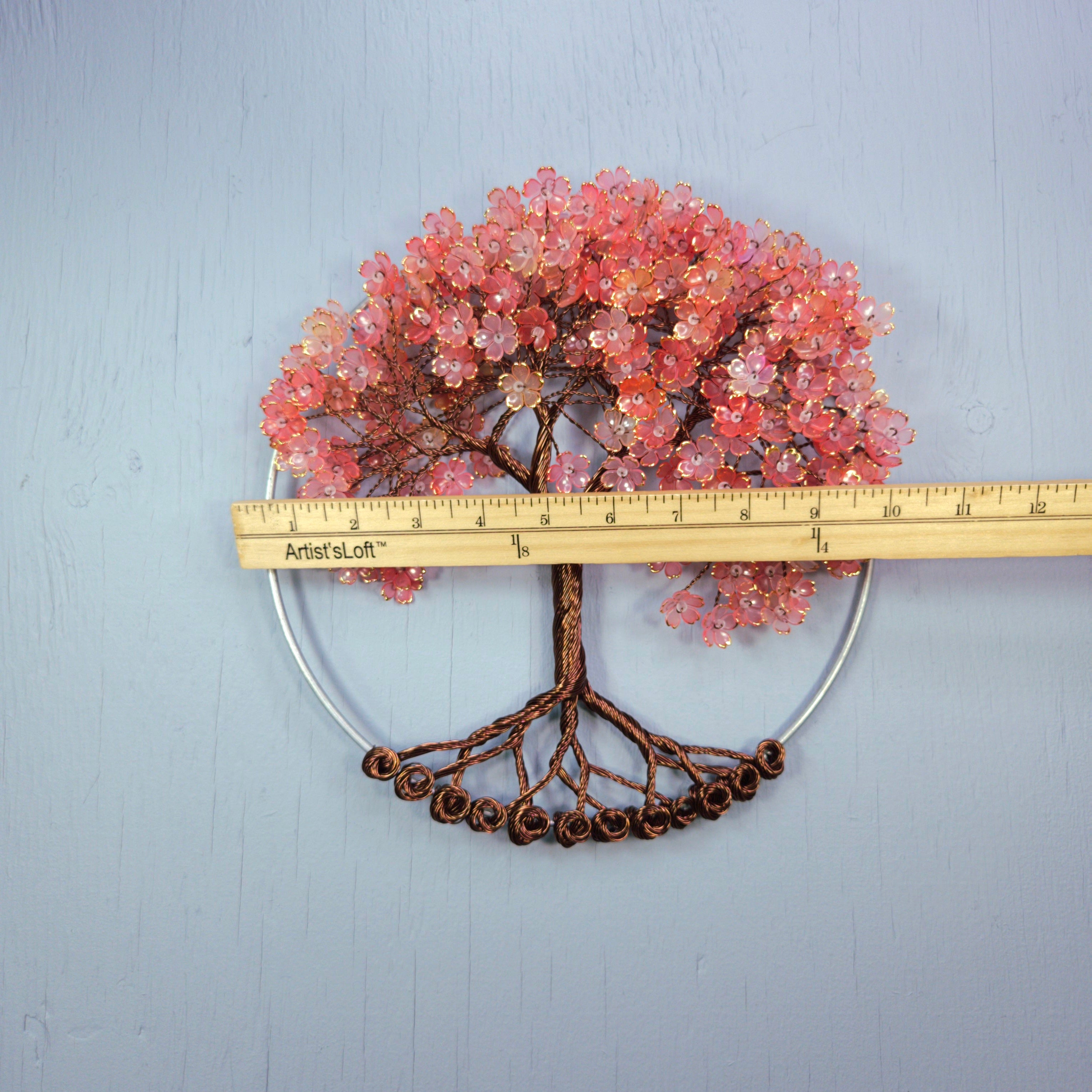 Decorative tree wall art with pink beads and a ruler for scale on a light gray background