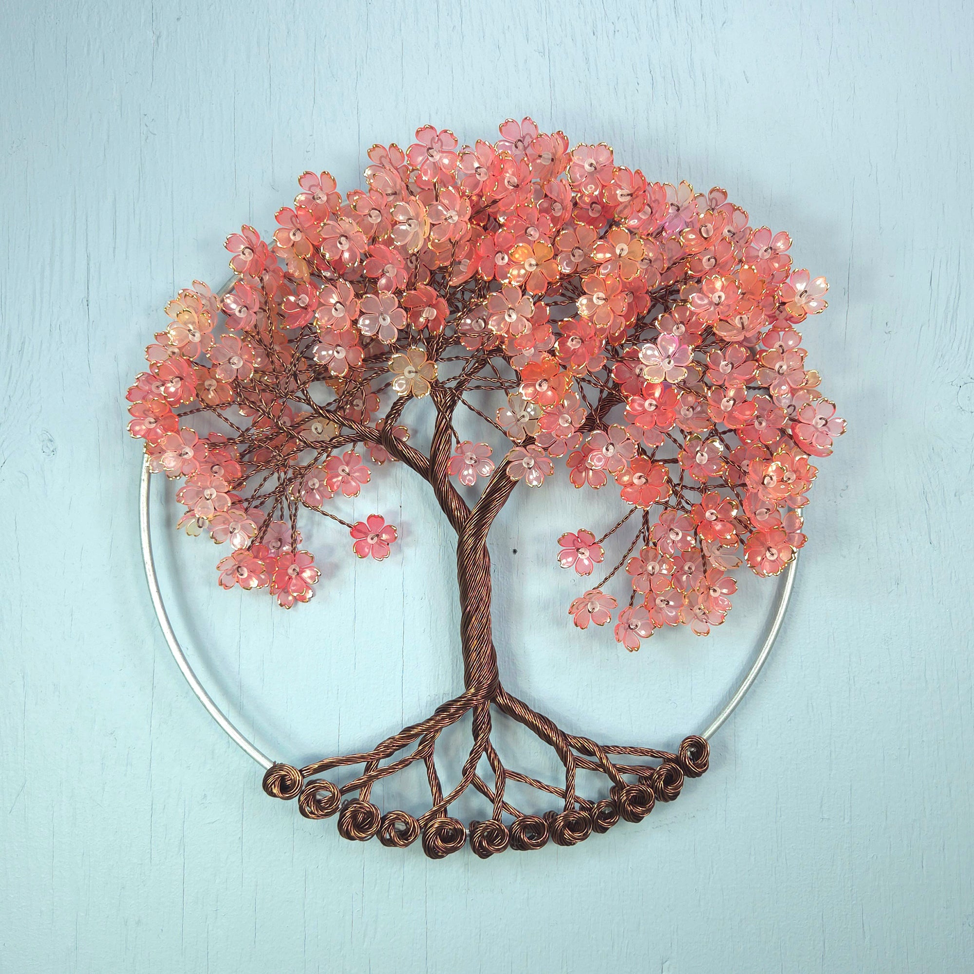 Decorative wall art of a tree with pink blossoms on a light blue background