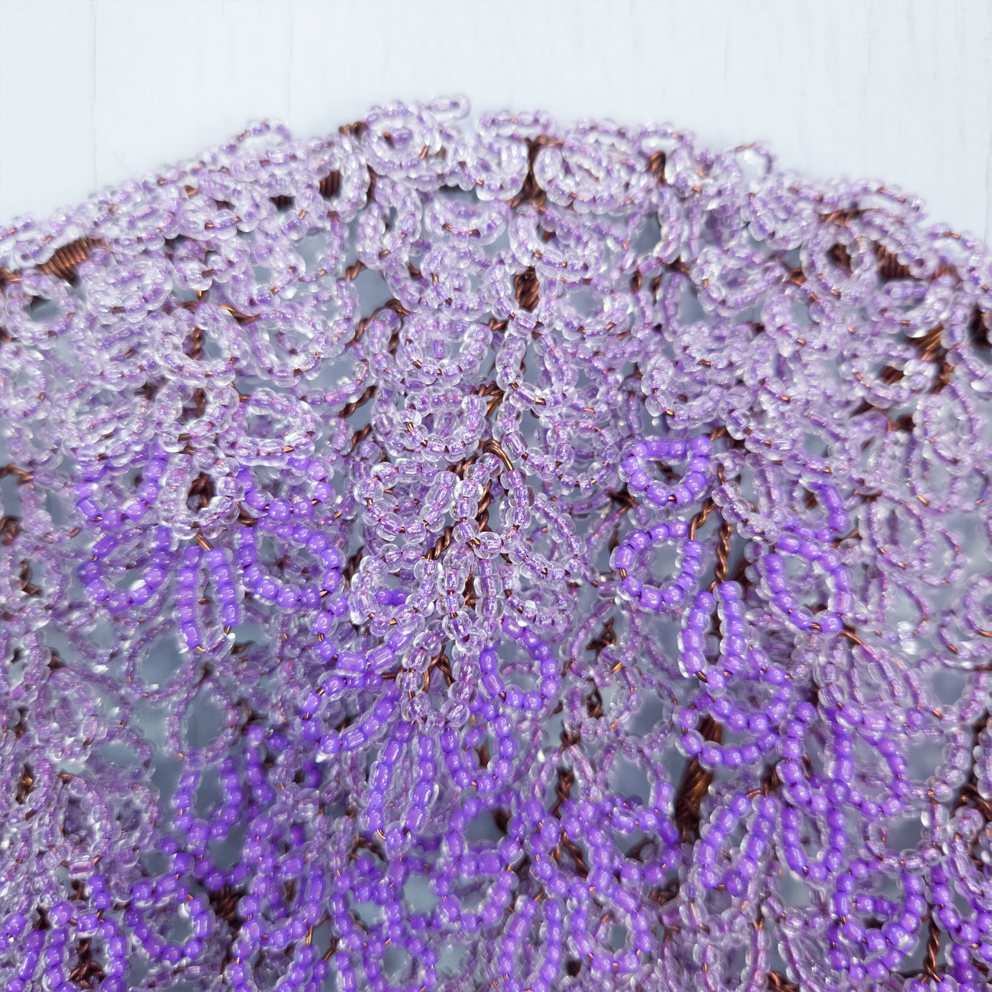 Close-up of a purple beaded lace fabric on a white background