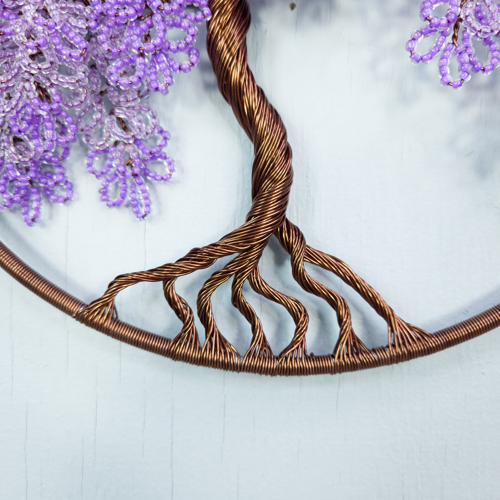 Decorative wreath with twisted copper wire design and purple flowers on a light blue background