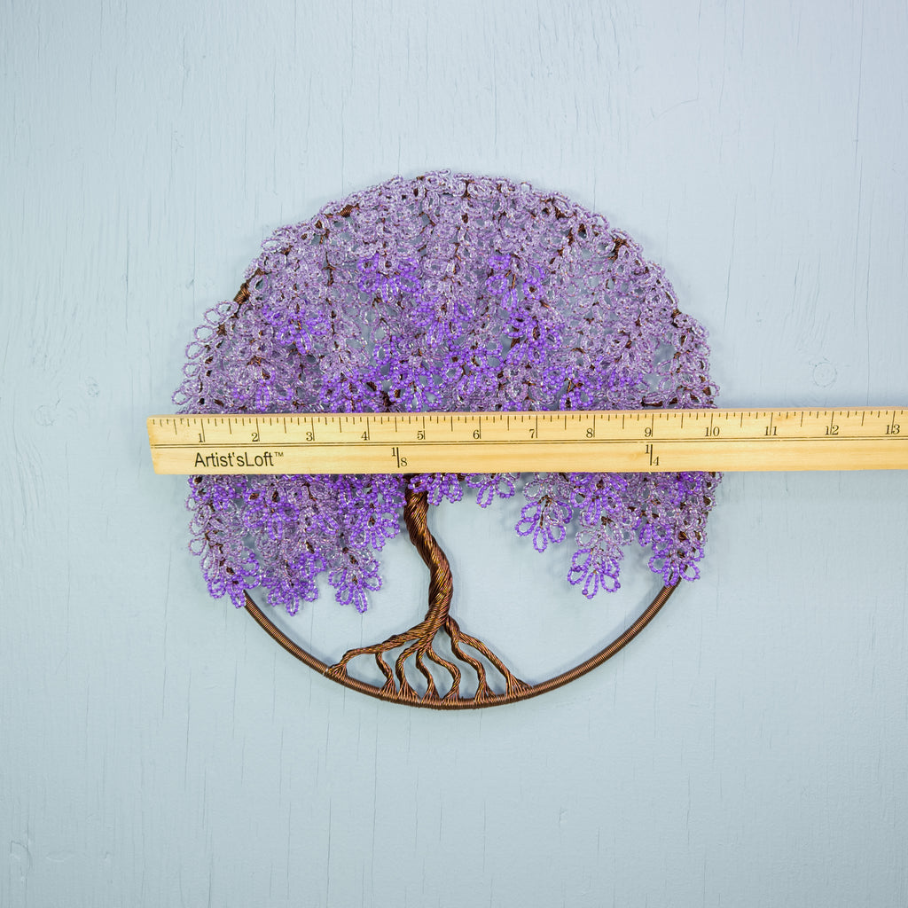 Decorative metal wall art of a tree with purple flowers and roots, measured against a ruler.