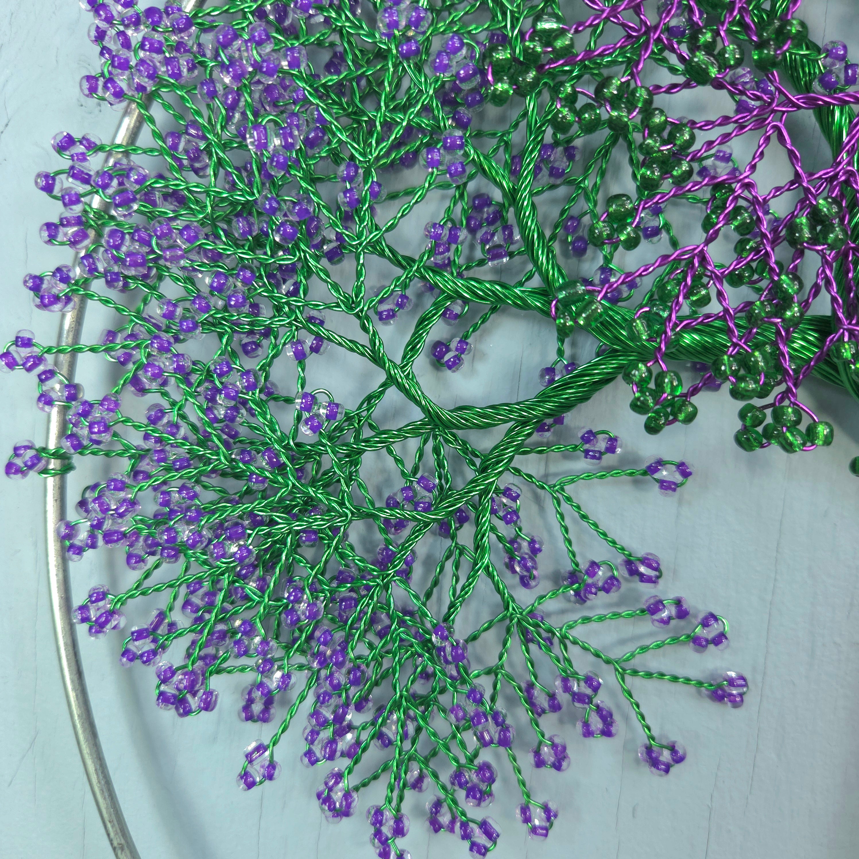Embroidery hoop with green and purple beaded branches on a light gray background
