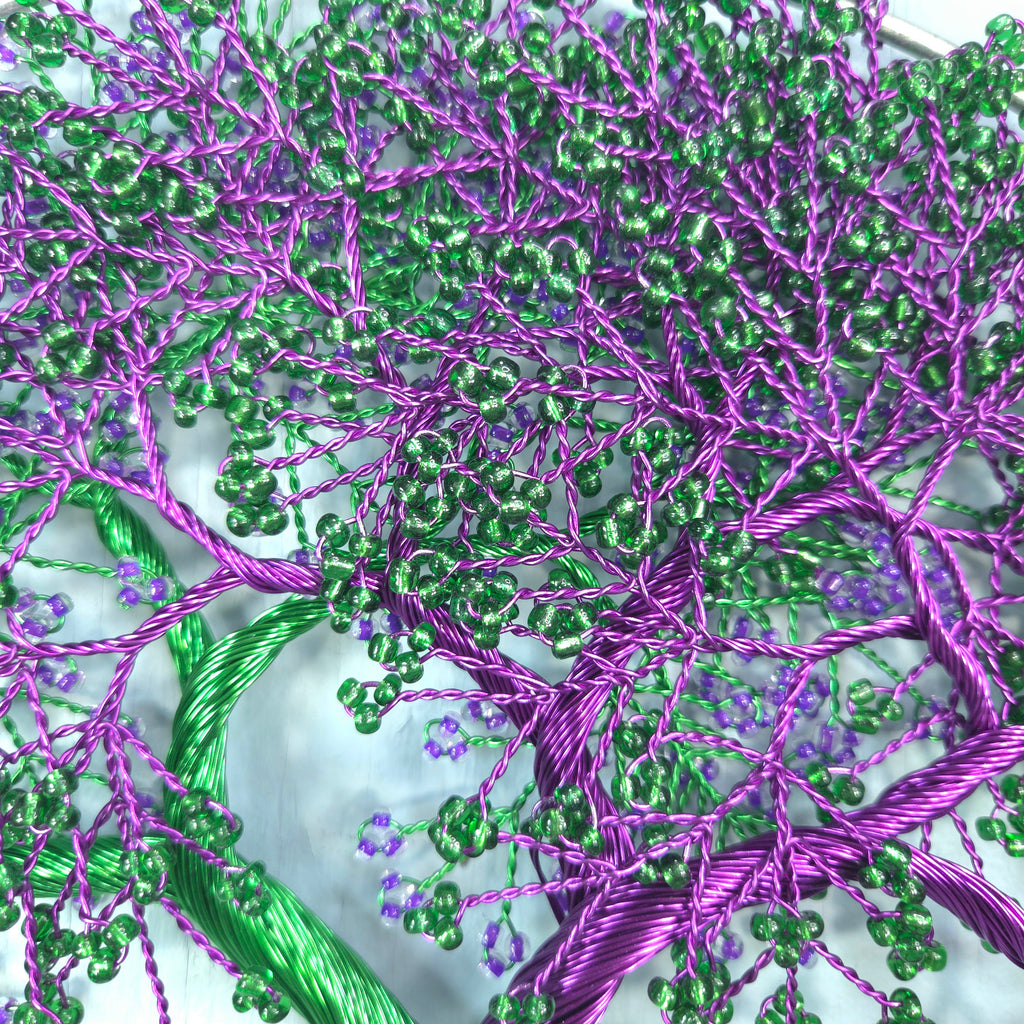 Close-up of intricate beadwork with purple and green threads on a textured surface.