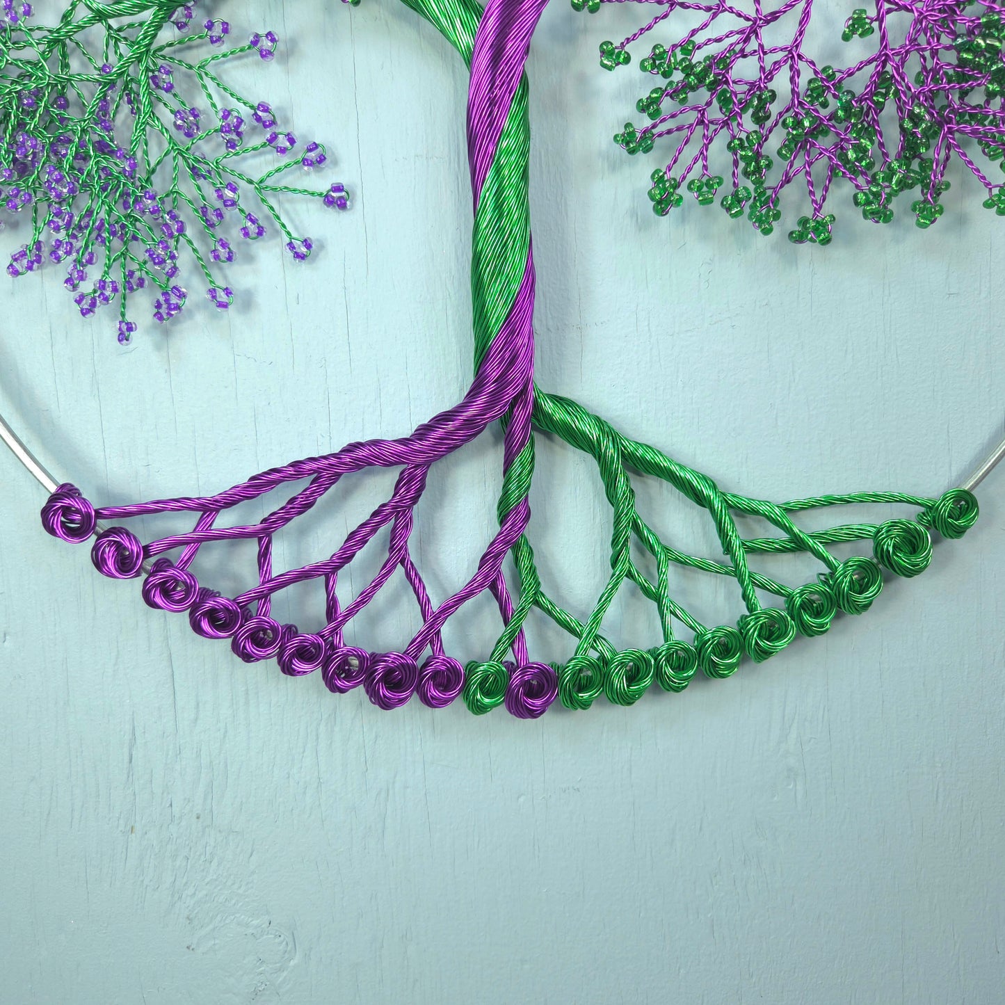 Embroidery of a tree with purple and green threads on a light background