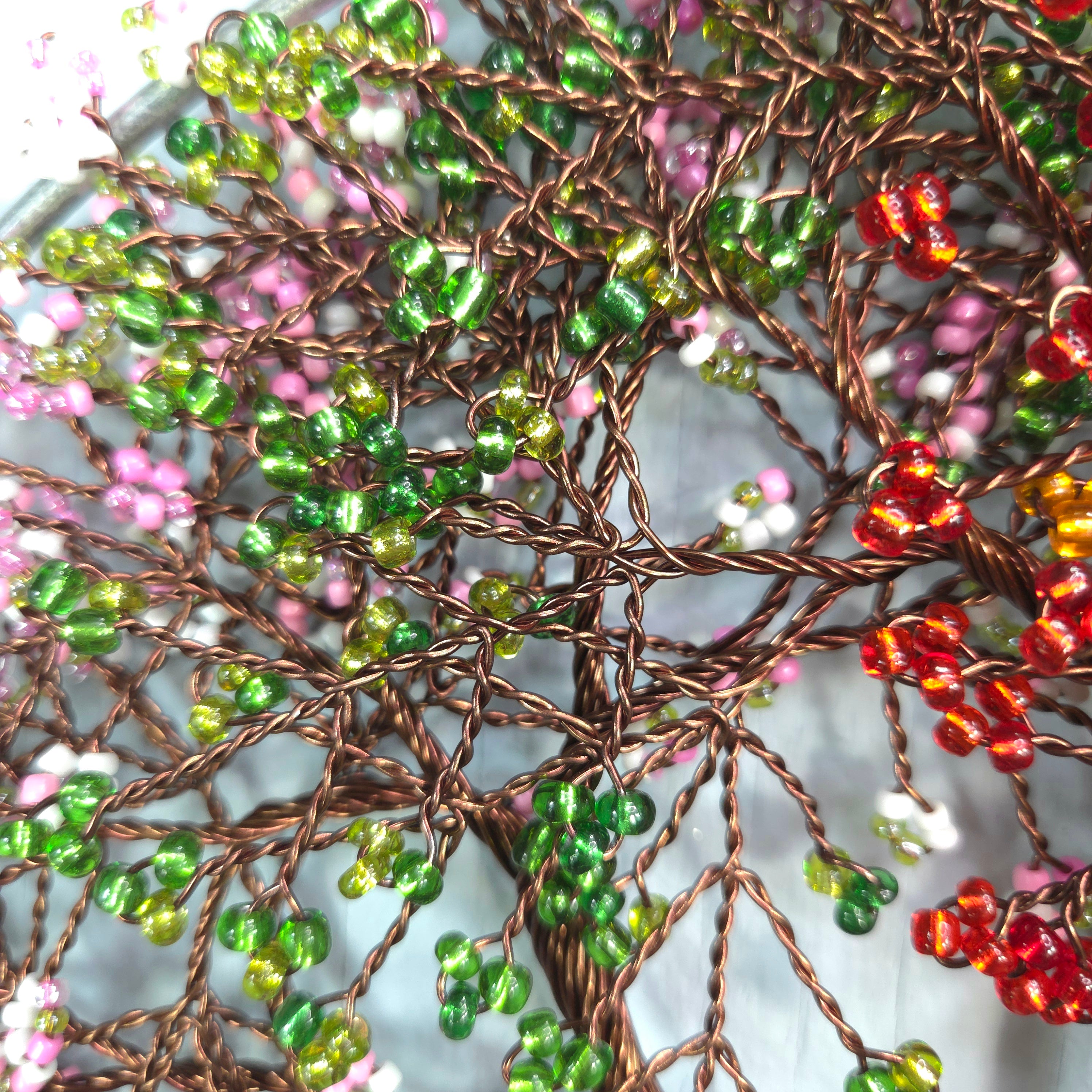 Close-up of a beaded tree art piece with green, red, and pink beads on a textured background.