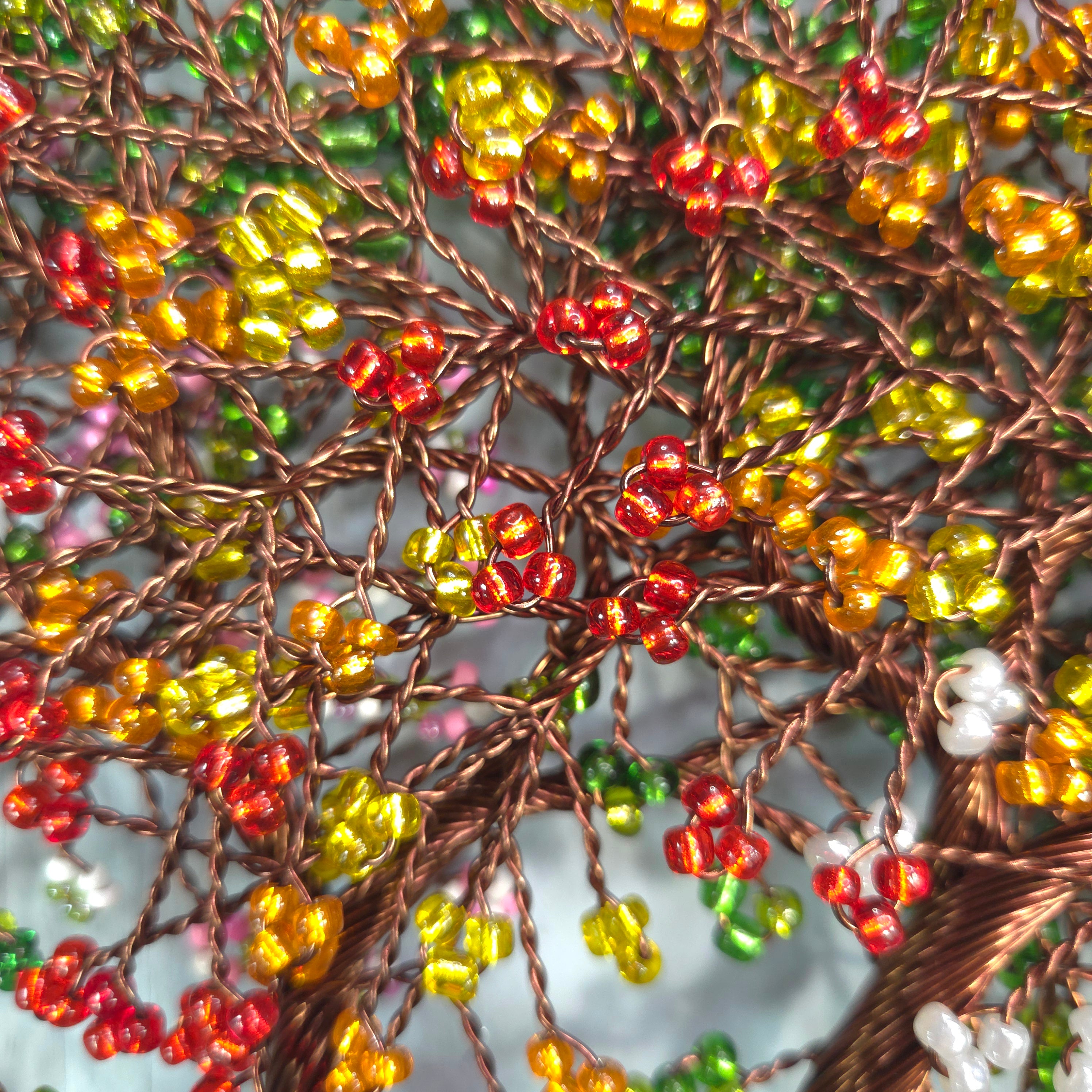 Close-up of a beaded tree with red, yellow, and green beads on a white background