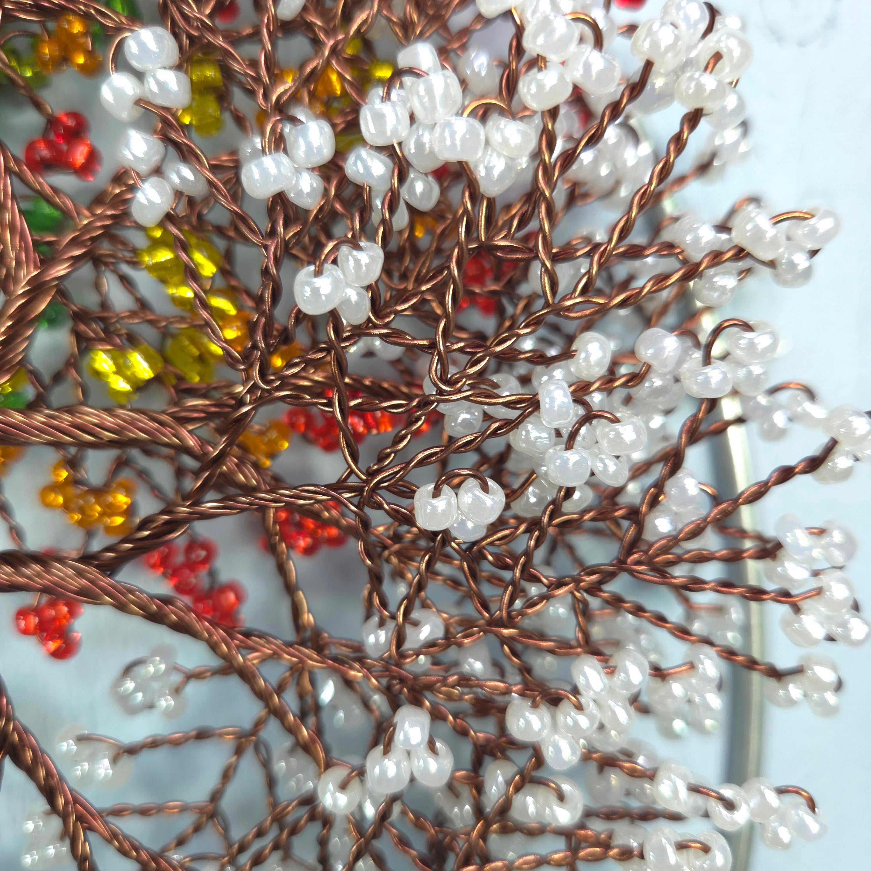 Close-up of a beaded tree with white beads and red and yellow accents on a light blue background.