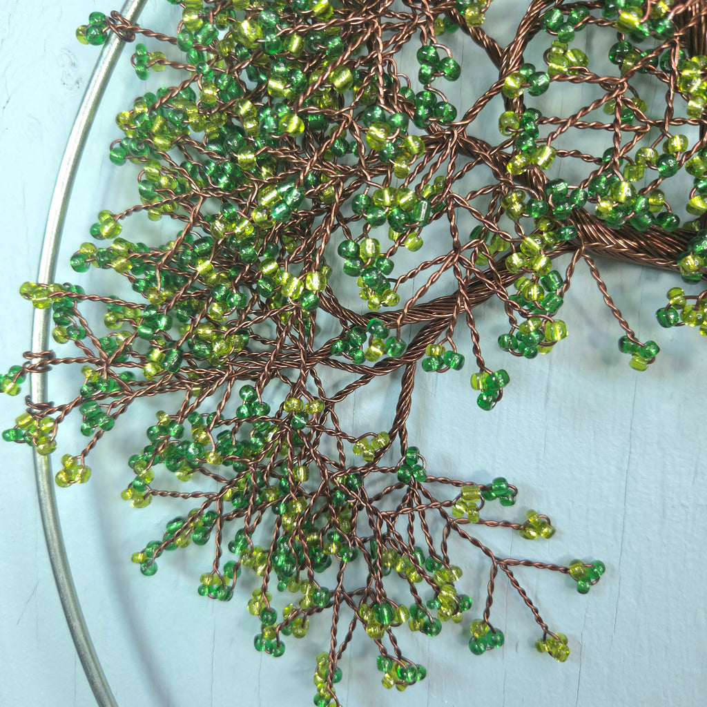 Decorative wreath with green beads and brown wire on a light blue background