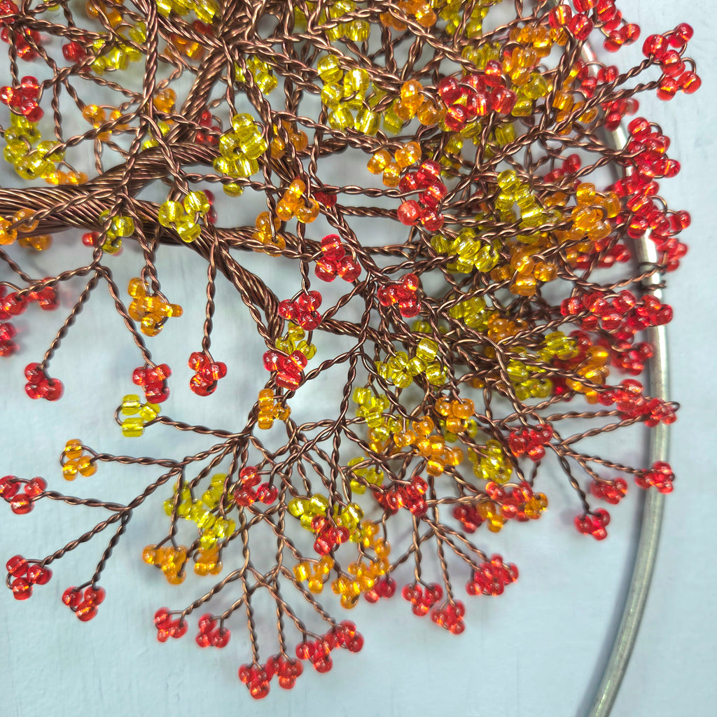 Decorative branch with red, yellow, and orange beads on a light blue background