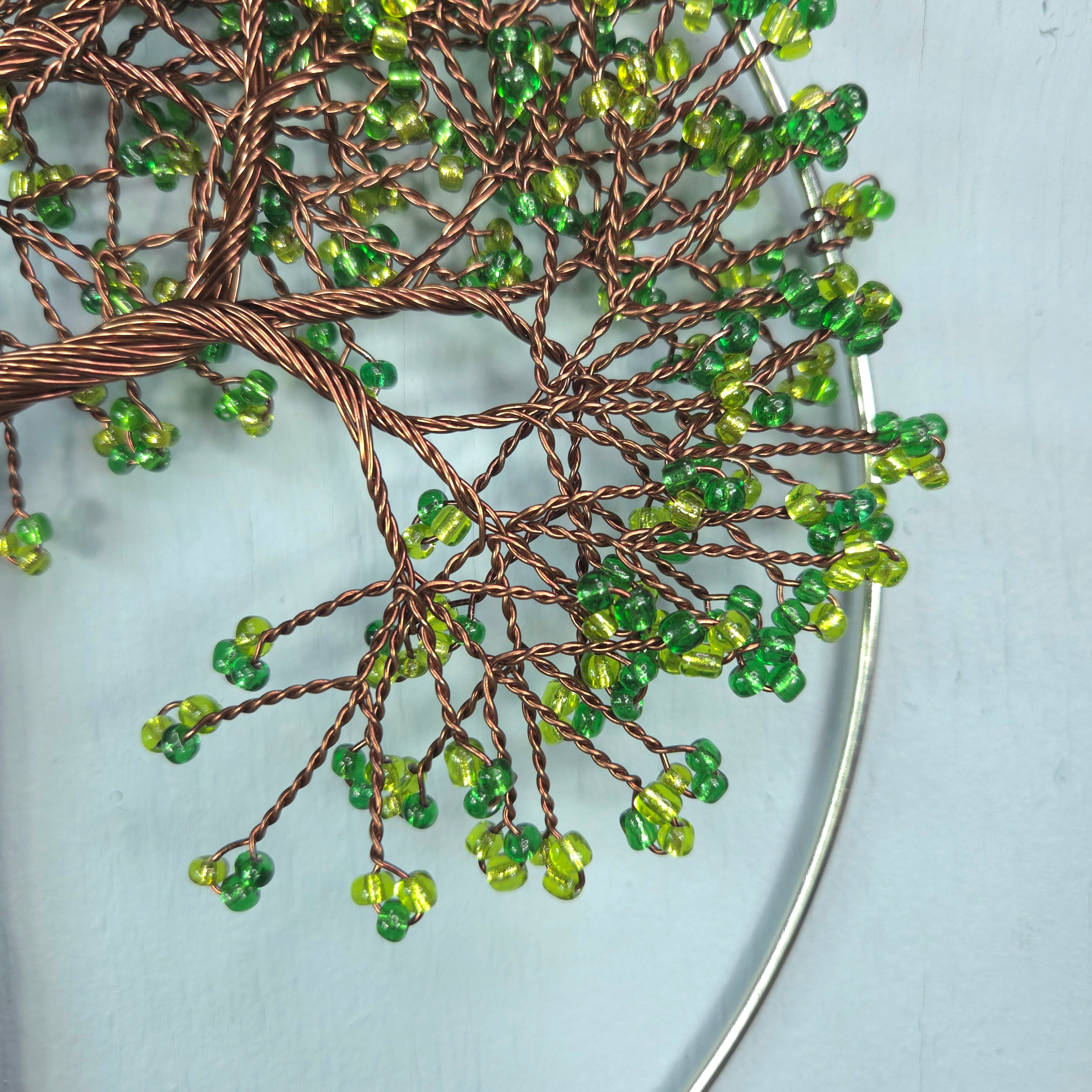 Decorative wall art with green beads and brown wire on a light blue background