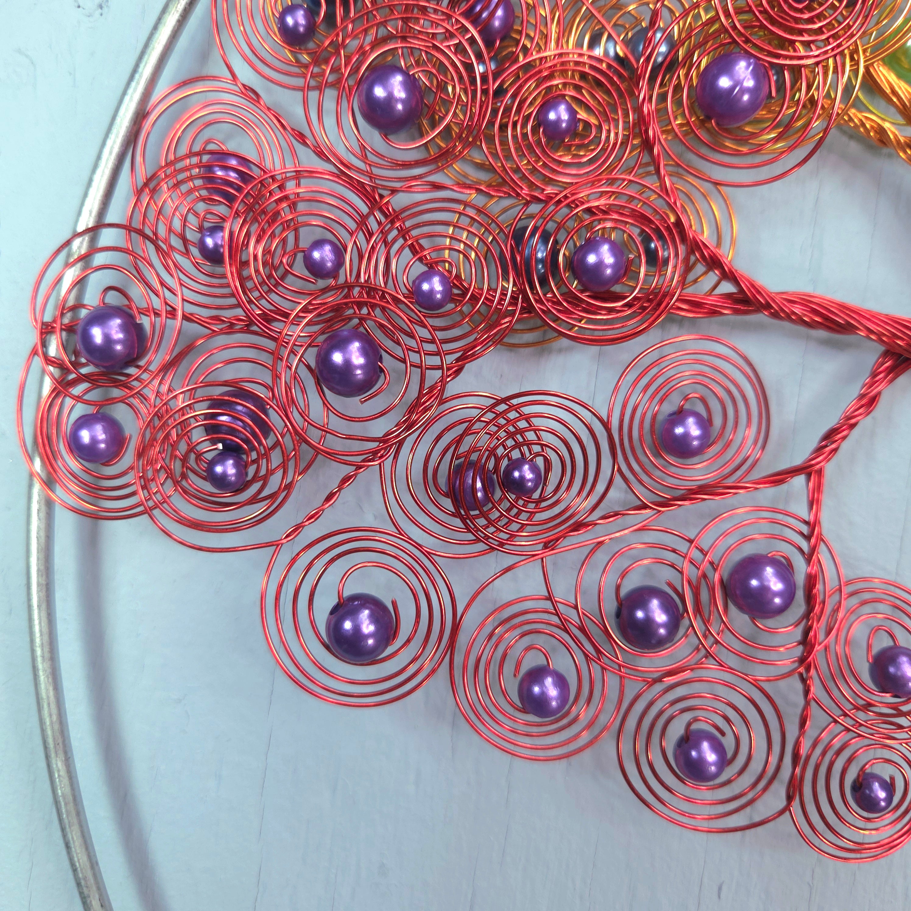Decorative wreath with copper wire and purple beads on a light blue background
