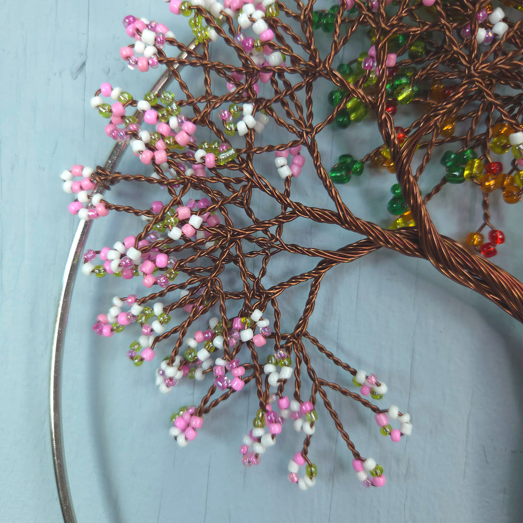 Decorative wall art with wire tree branches and colorful beads on a light blue background