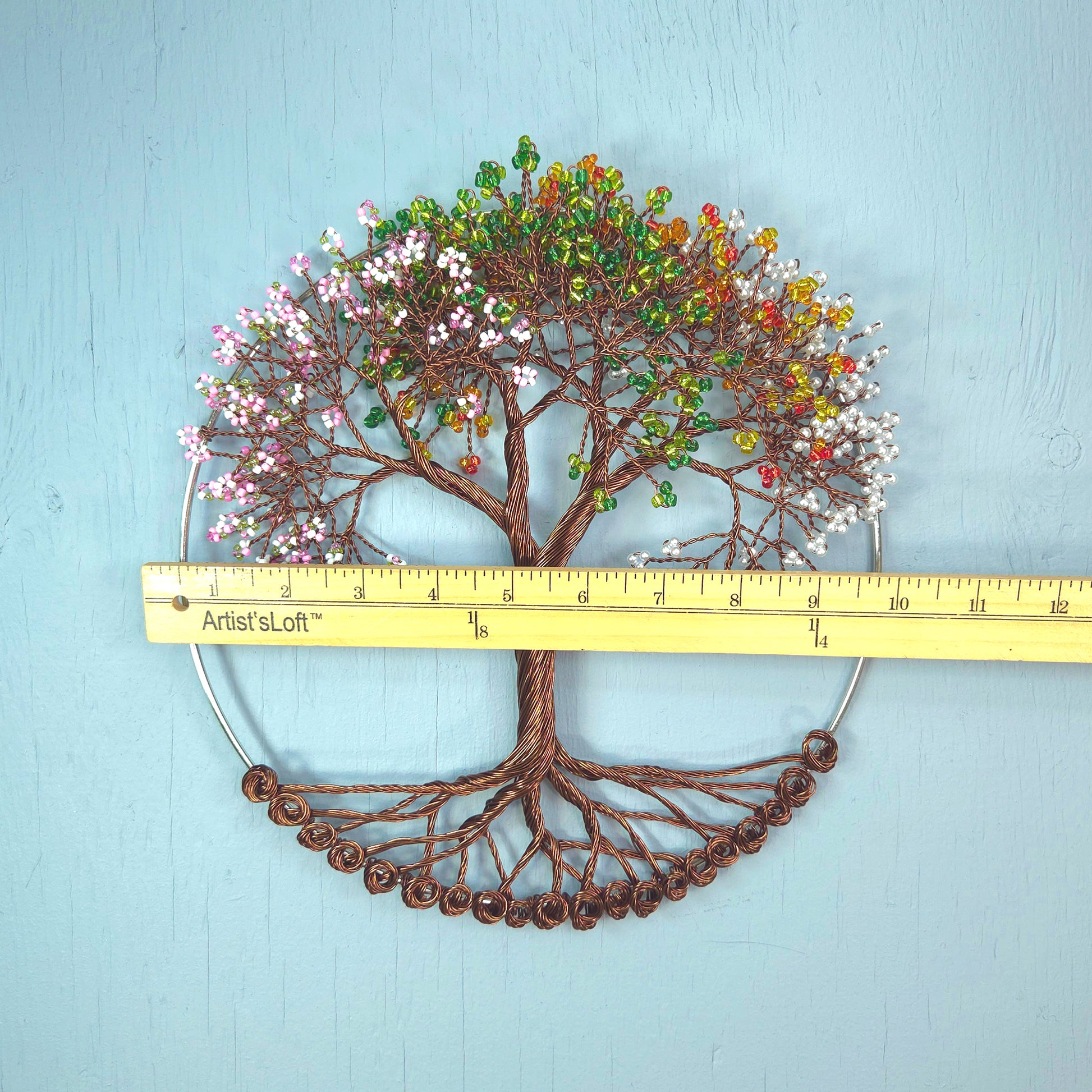 Decorative tree wall art with colorful leaves and a ruler for scale on a light blue background