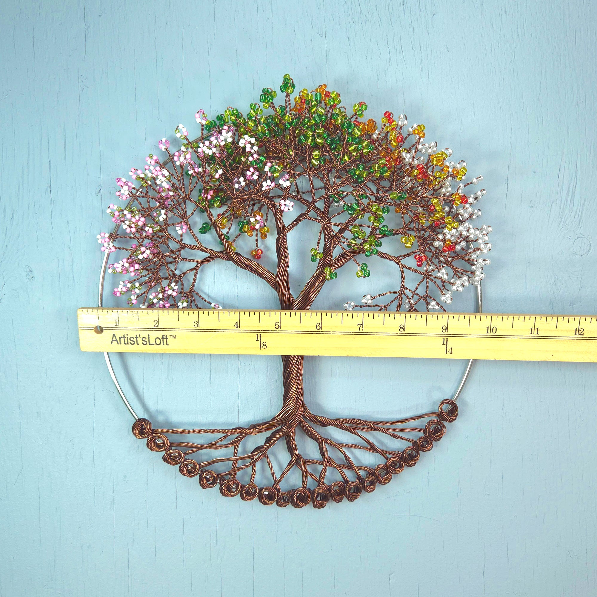 Decorative tree wall art with colorful leaves and a ruler for scale on a light blue background