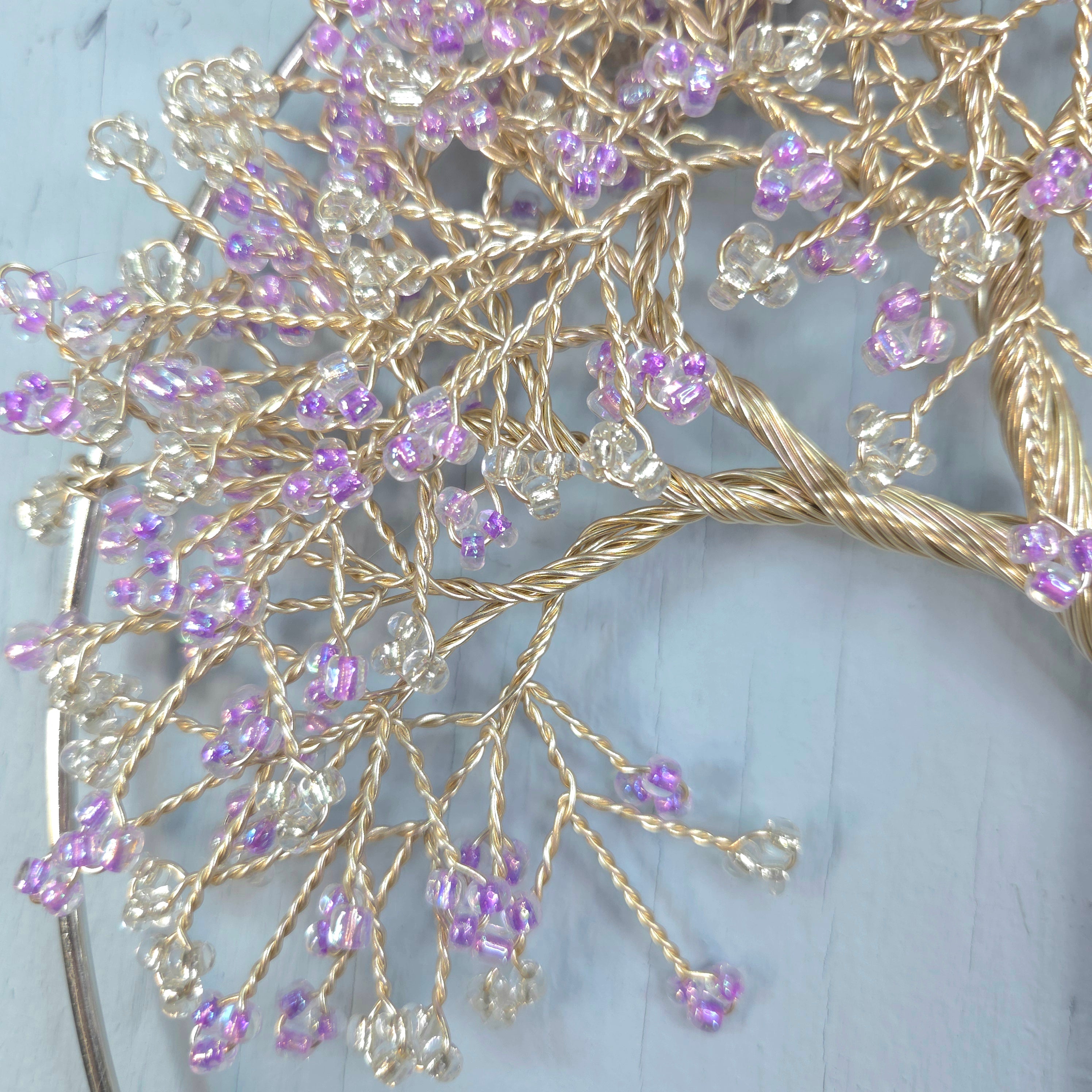 Decorative hairpin with gold branches and purple beads on a light blue background